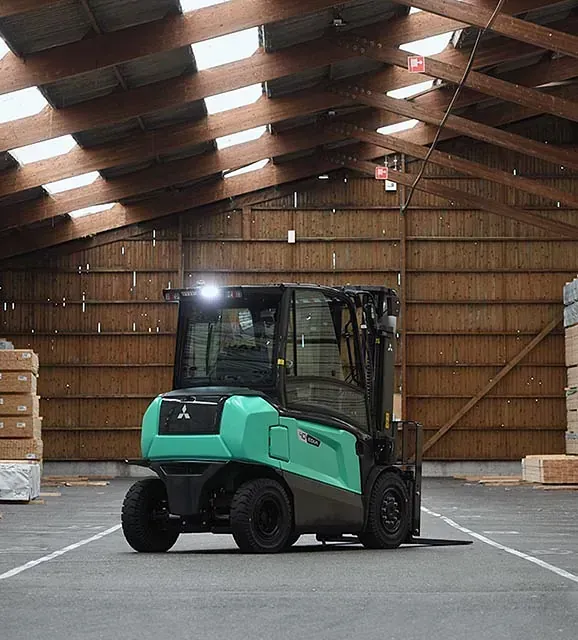 Una carretilla elevadora verde está estacionada en un gran almacén.