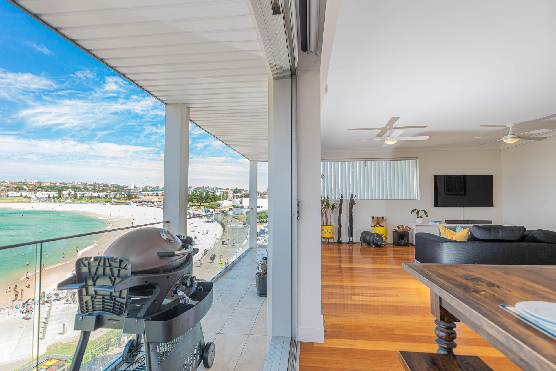 Balcony view of turquoise water with a barbecue grill beside a bright living room and kitchen.
