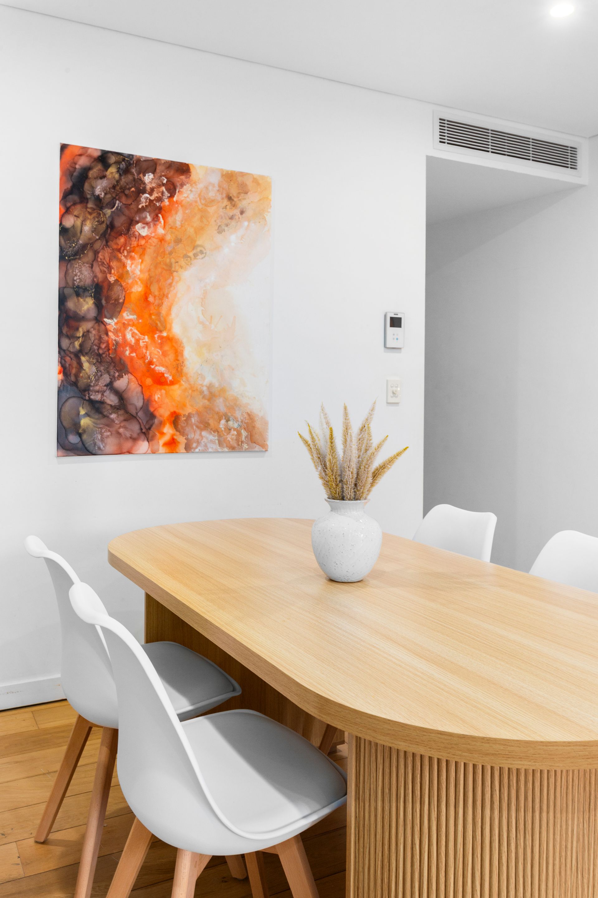 Modern dining room with a wood table, white chairs, abstract wall art, and a vase centerpiece