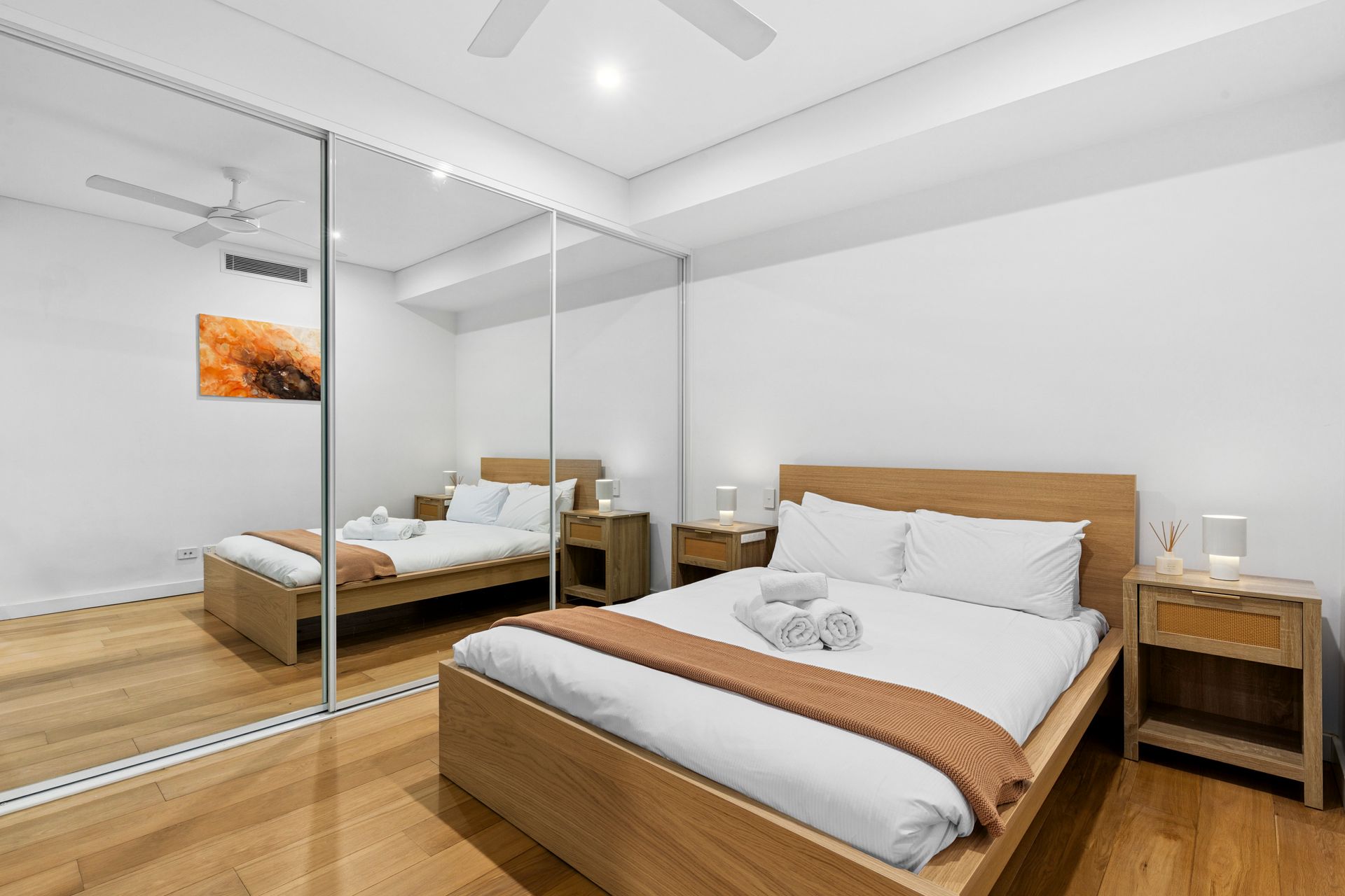 Modern bedroom with wooden bed, mirrored closet doors, and warm wood flooring