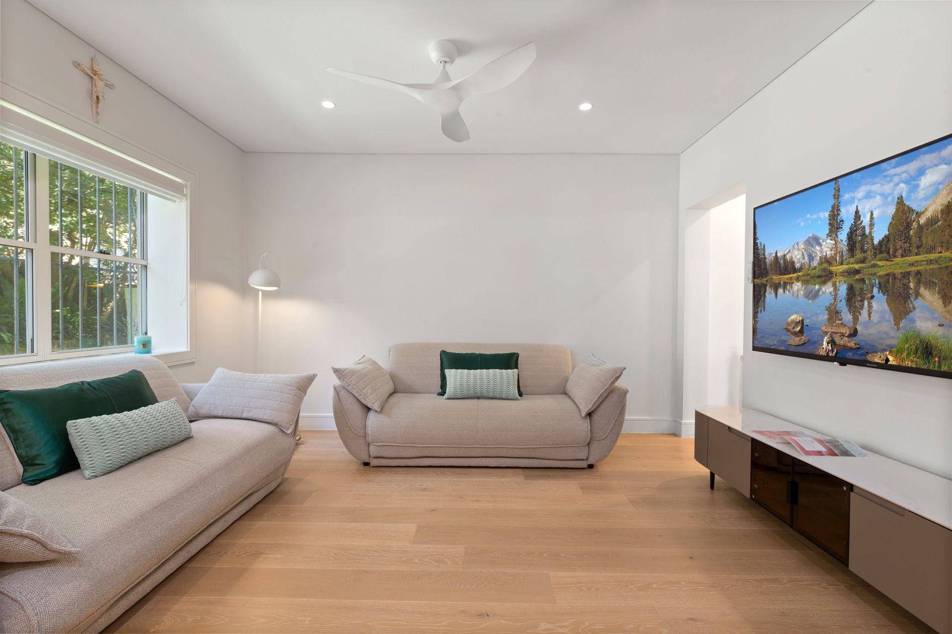 Bright living room with two gray sofas, wood floor, wall-mounted TV, and large windows.