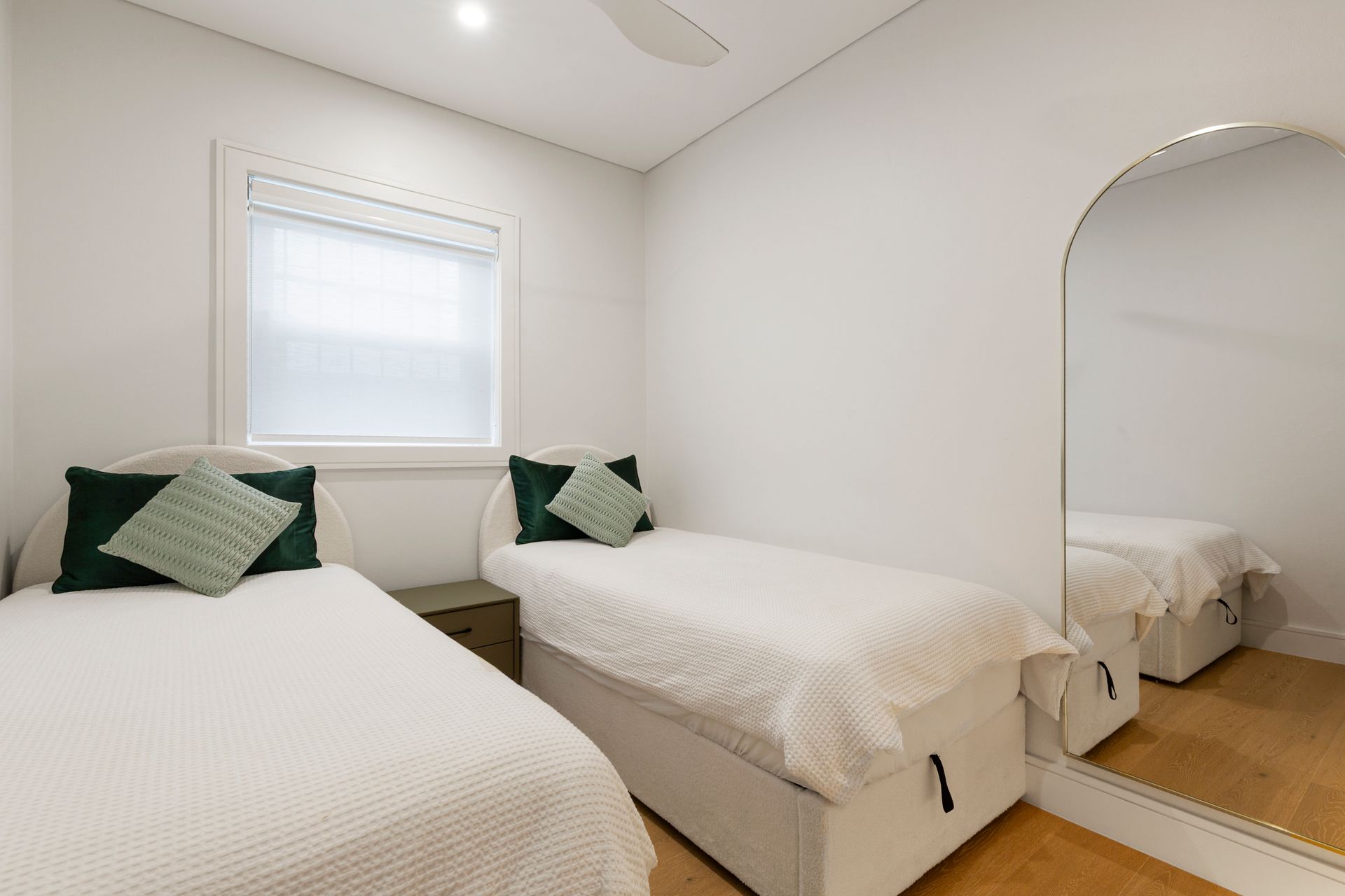 Bright bedroom with two white beds, green pillows, and a large mirror by the wall
