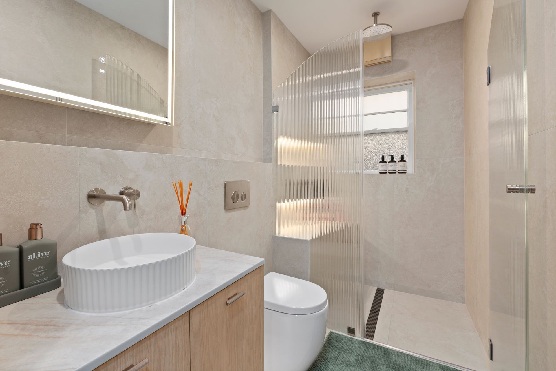 Modern bathroom with round vessel sink, toilet, shower, and green bath mat