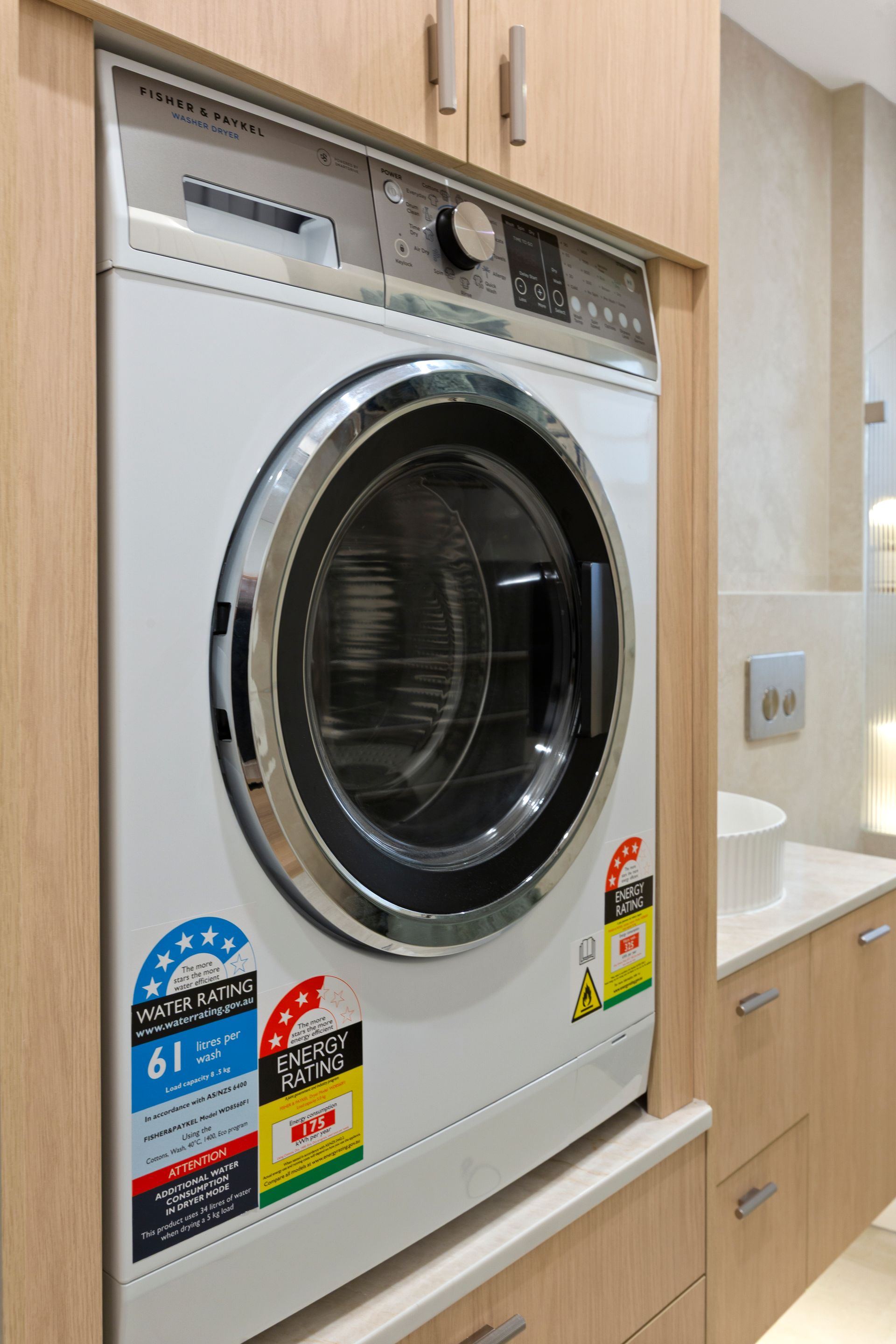 Front-loading washer-dryer in a light wood laundry alcove next to a sink and cabinet.
