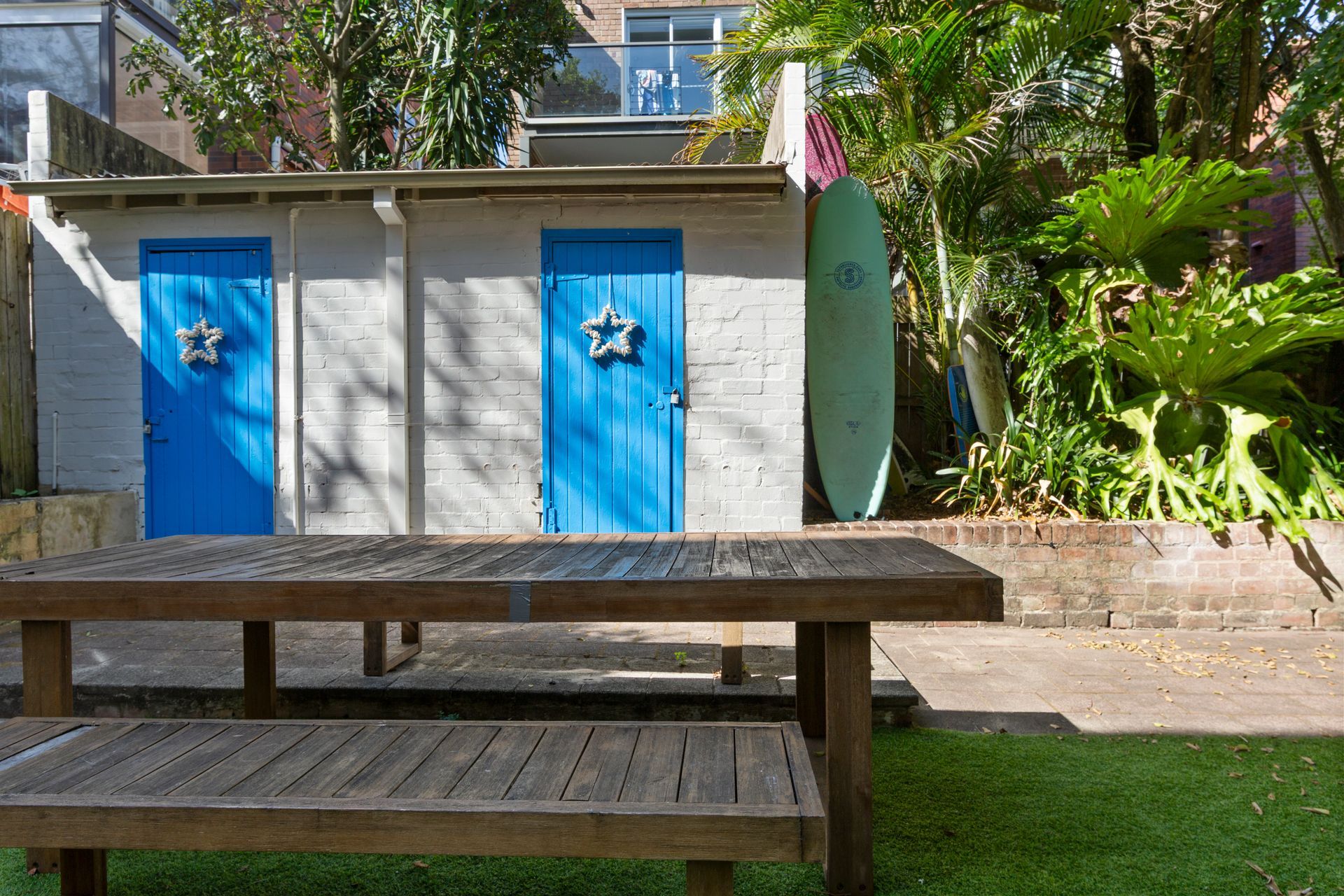 Outdoor restroom building with blue doors beside a picnic table and green plants