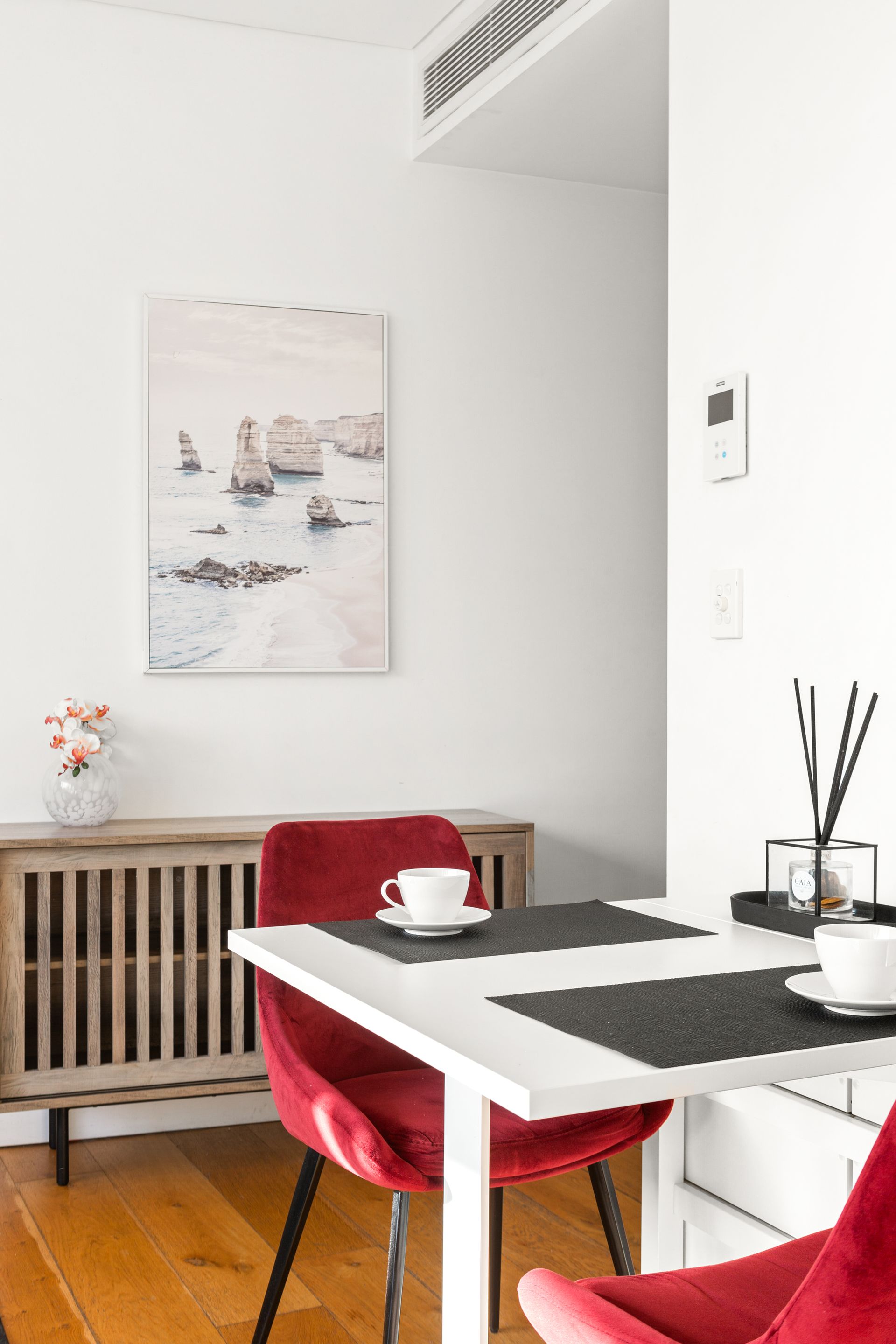 Bright dining nook with red chairs, white table, framed art, and a radiator under the window.