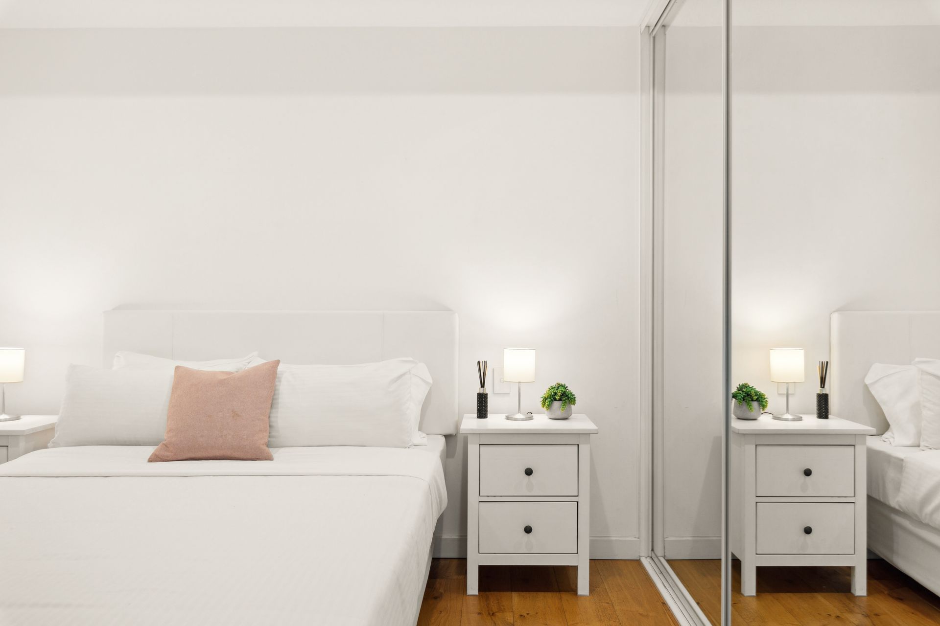 Minimal white bedroom with a bed, bedside tables, and mirrored closet doors.