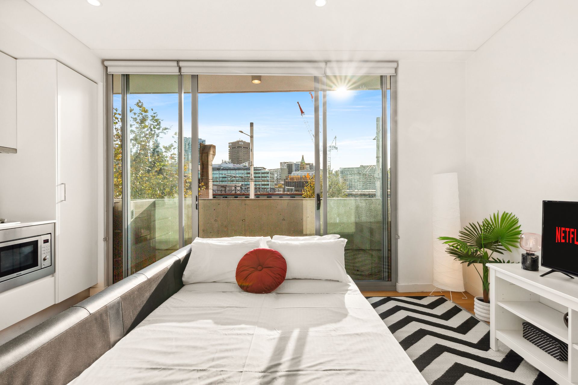 Bright white bedroom with bed, balcony windows, city view, and black-and-white rug