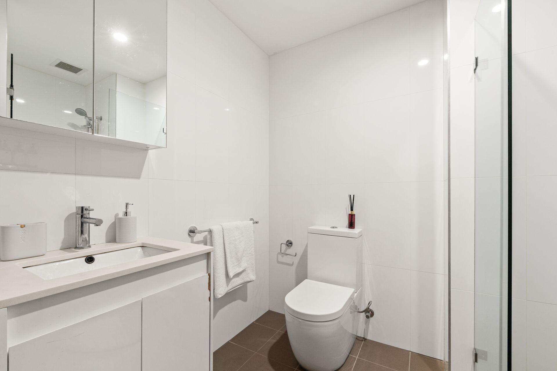 Modern white bathroom with vanity, mirror cabinet, toilet, towel rail, and glass shower enclosure