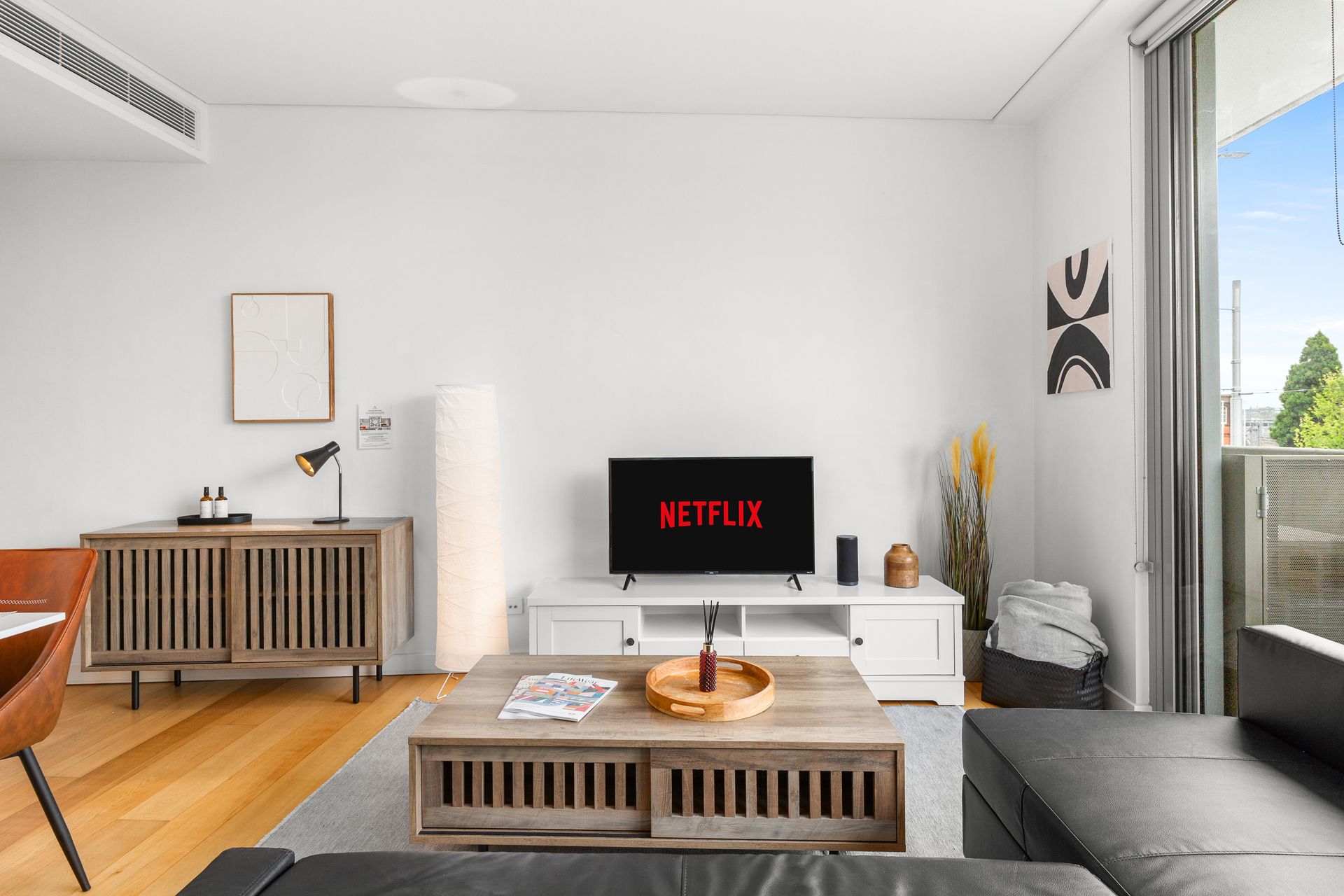 Bright living room with white walls, gray sofa, TV, coffee table, and wooden sideboard