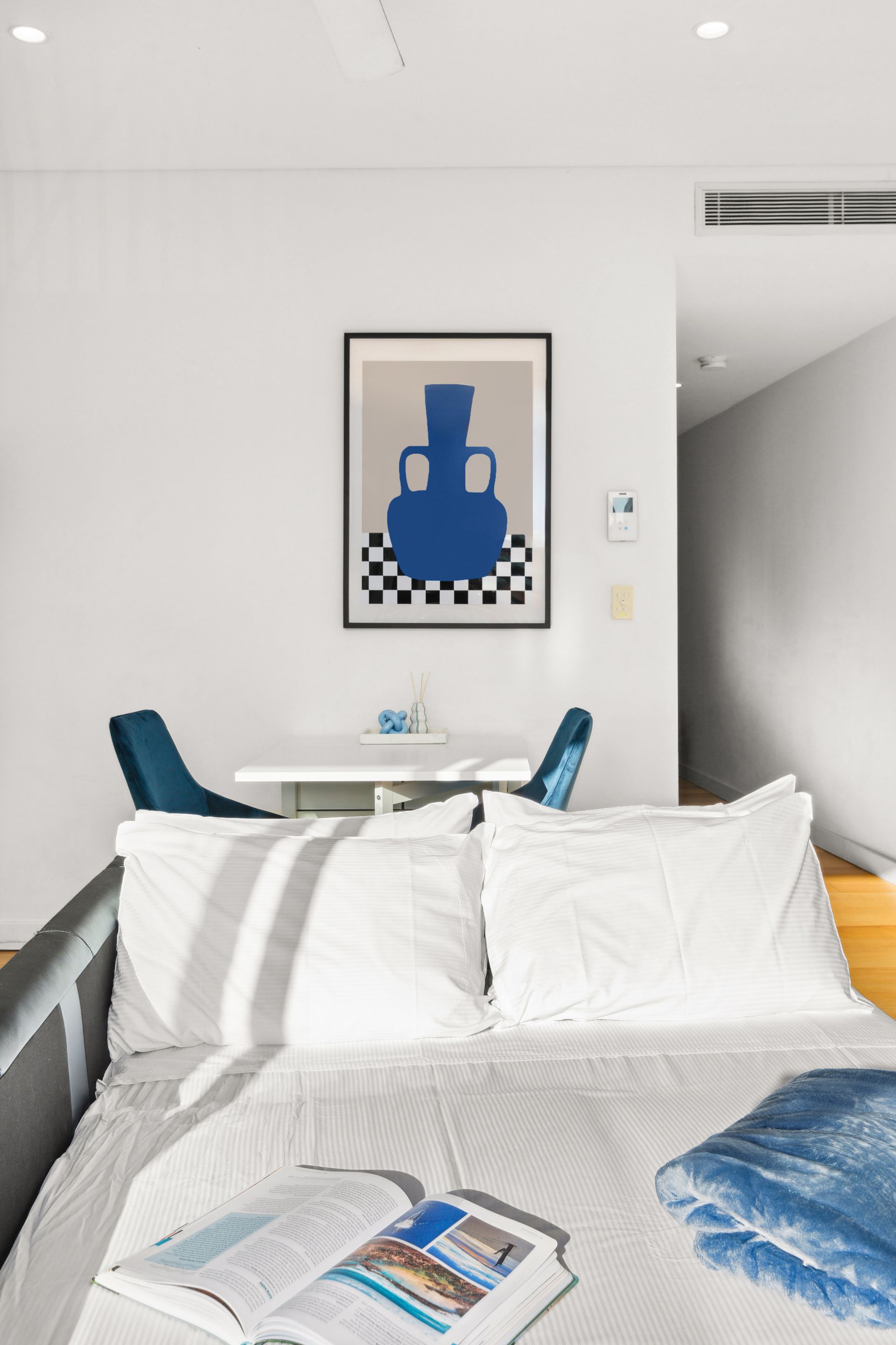 Bright bedroom with a bed, blue chairs, and framed abstract wall art