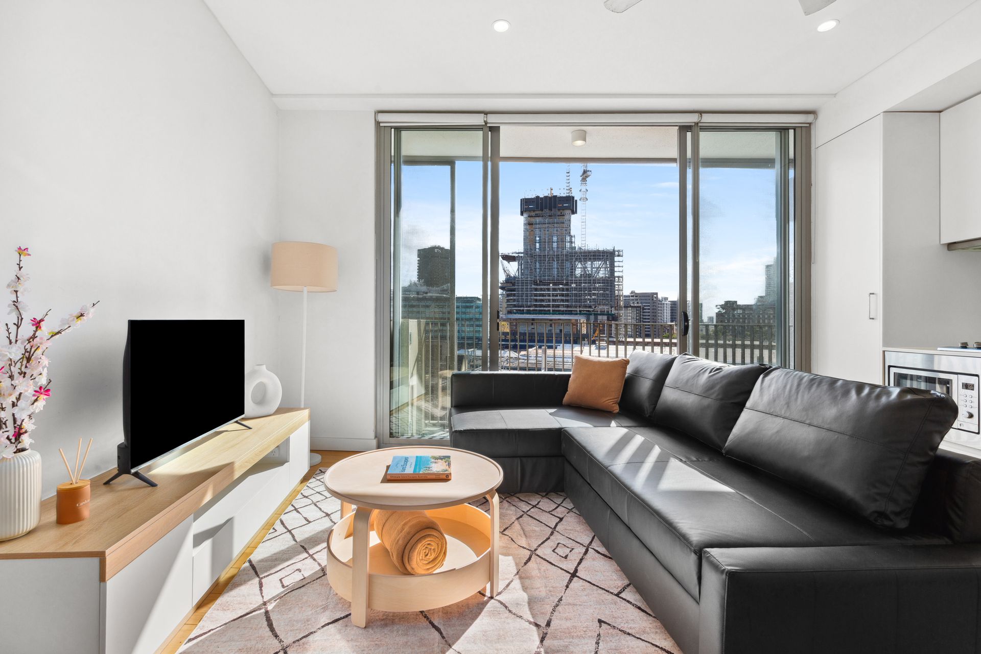 Modern living room with black sofa, round coffee table, TV console, and large windows overlooking a city view
