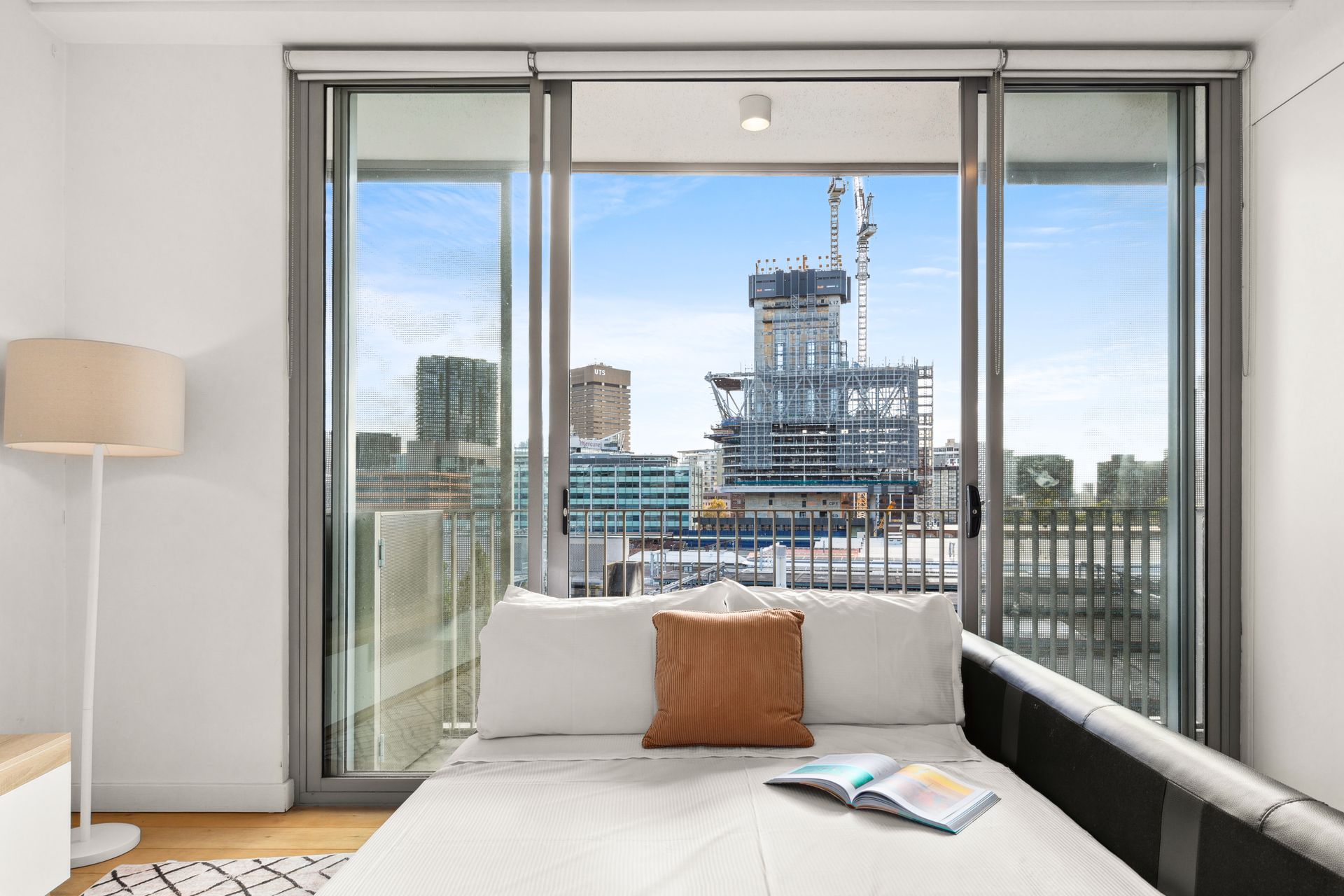 Bright bedroom with a white bed facing large windows and a city skyline outside