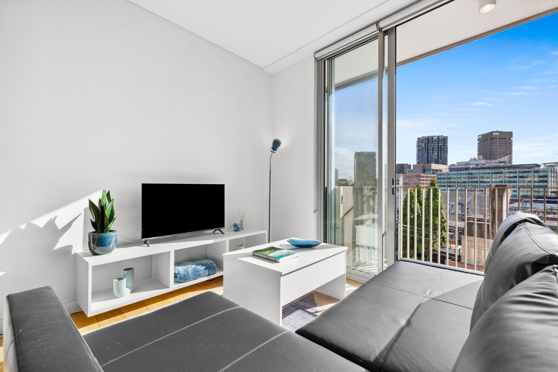 Modern living room with gray sofa, TV, and city view through large windows