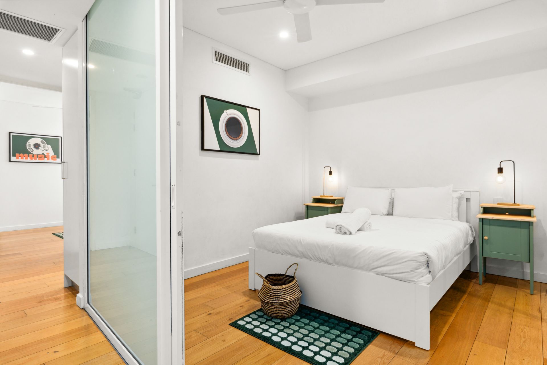 Bright bedroom with white bed, green nightstands, wooden floor, and glass sliding door