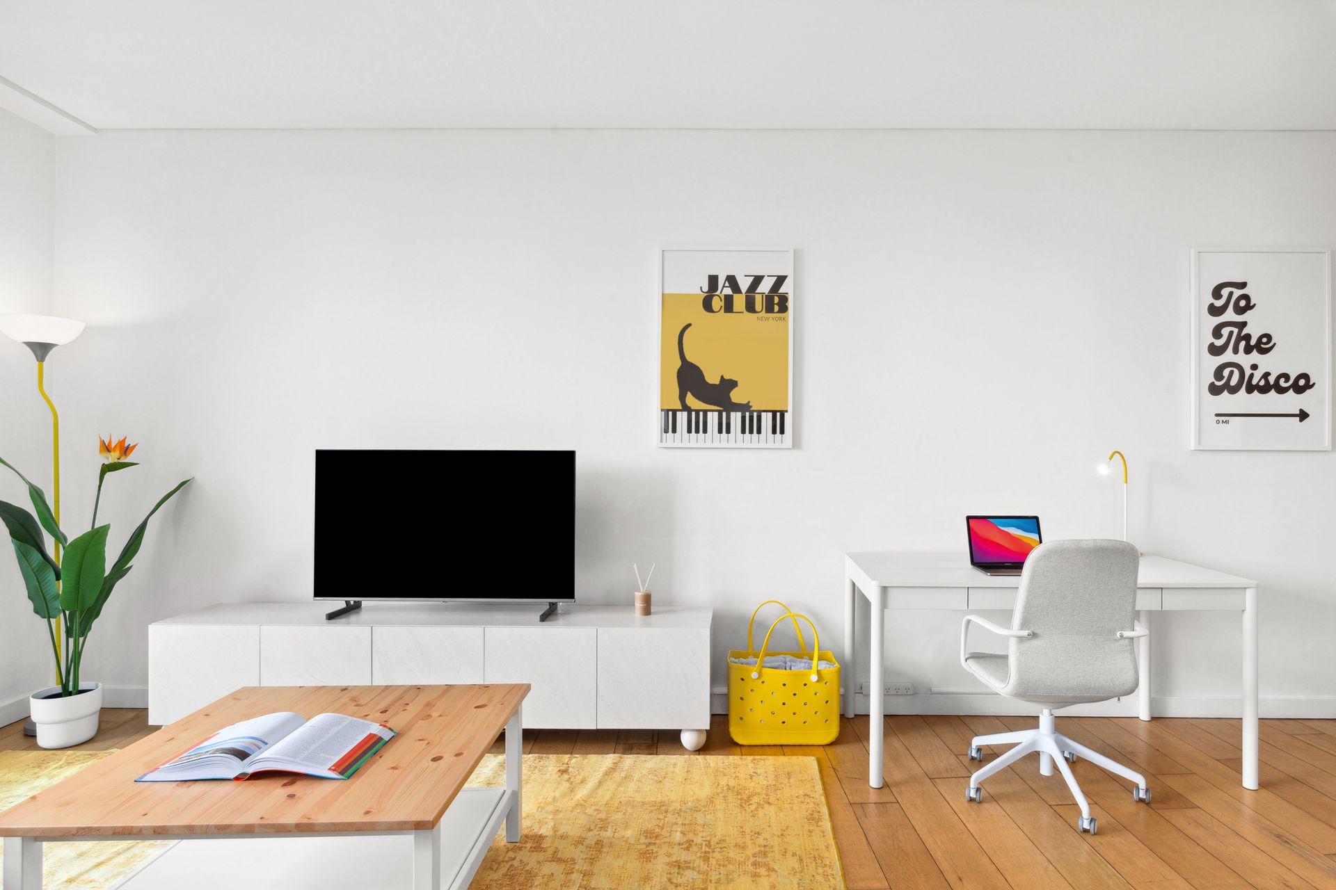Modern white living room with TV, sofa, desk, plant, and yellow storage bin
