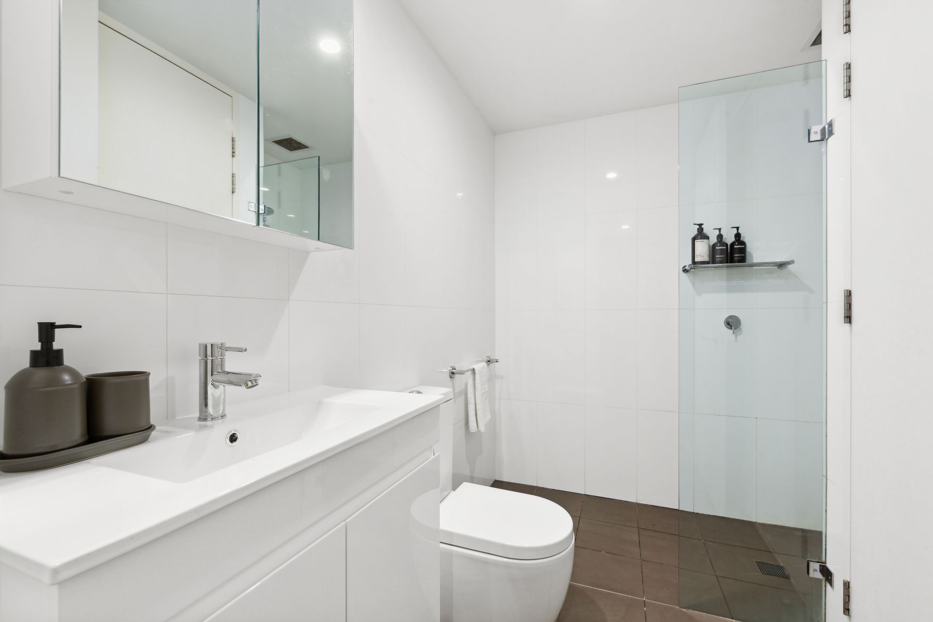 Modern white bathroom with vanity, toilet, glass shower, and dark tile floor