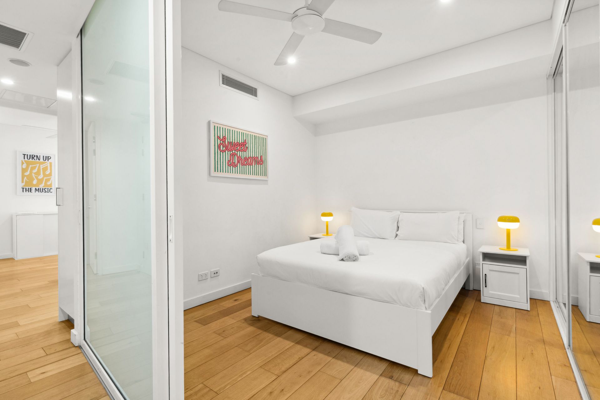 Minimal white bedroom with a bed, bedside lamps, wood floor, and sliding glass partition