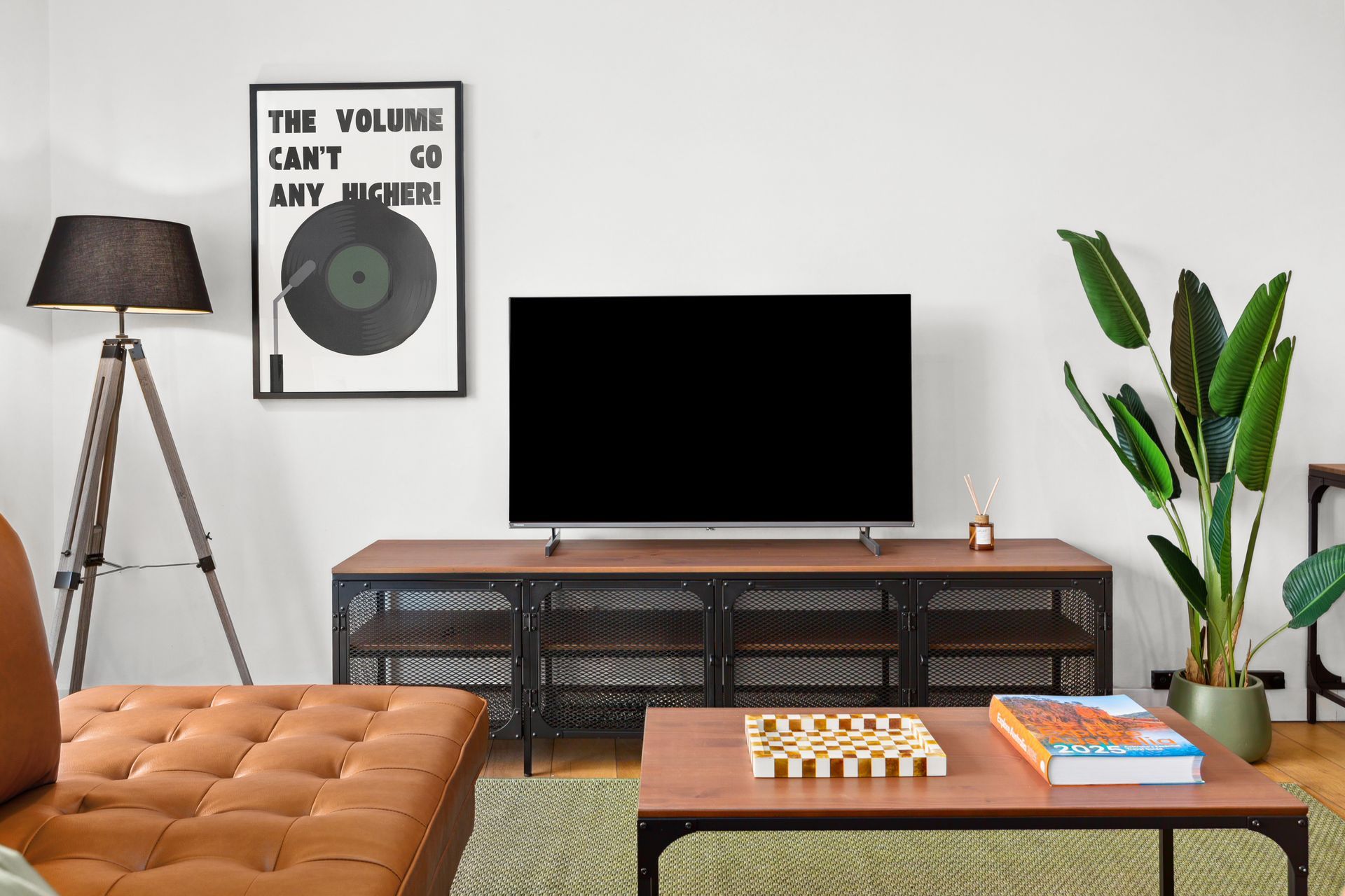 Modern living room with TV on a console, tan tufted sofa, floor lamp, coffee table, and tall plant.
