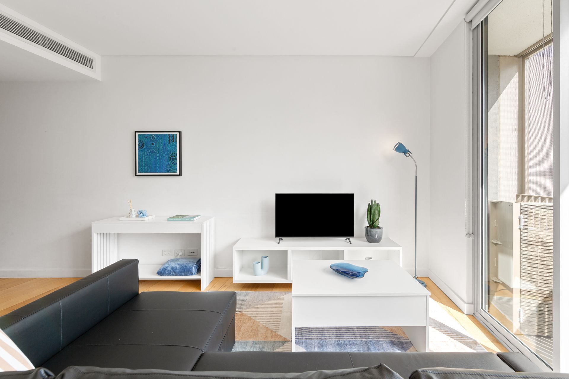 Bright modern living room with black sofa, white furniture, TV, and sliding glass doors to a balcony