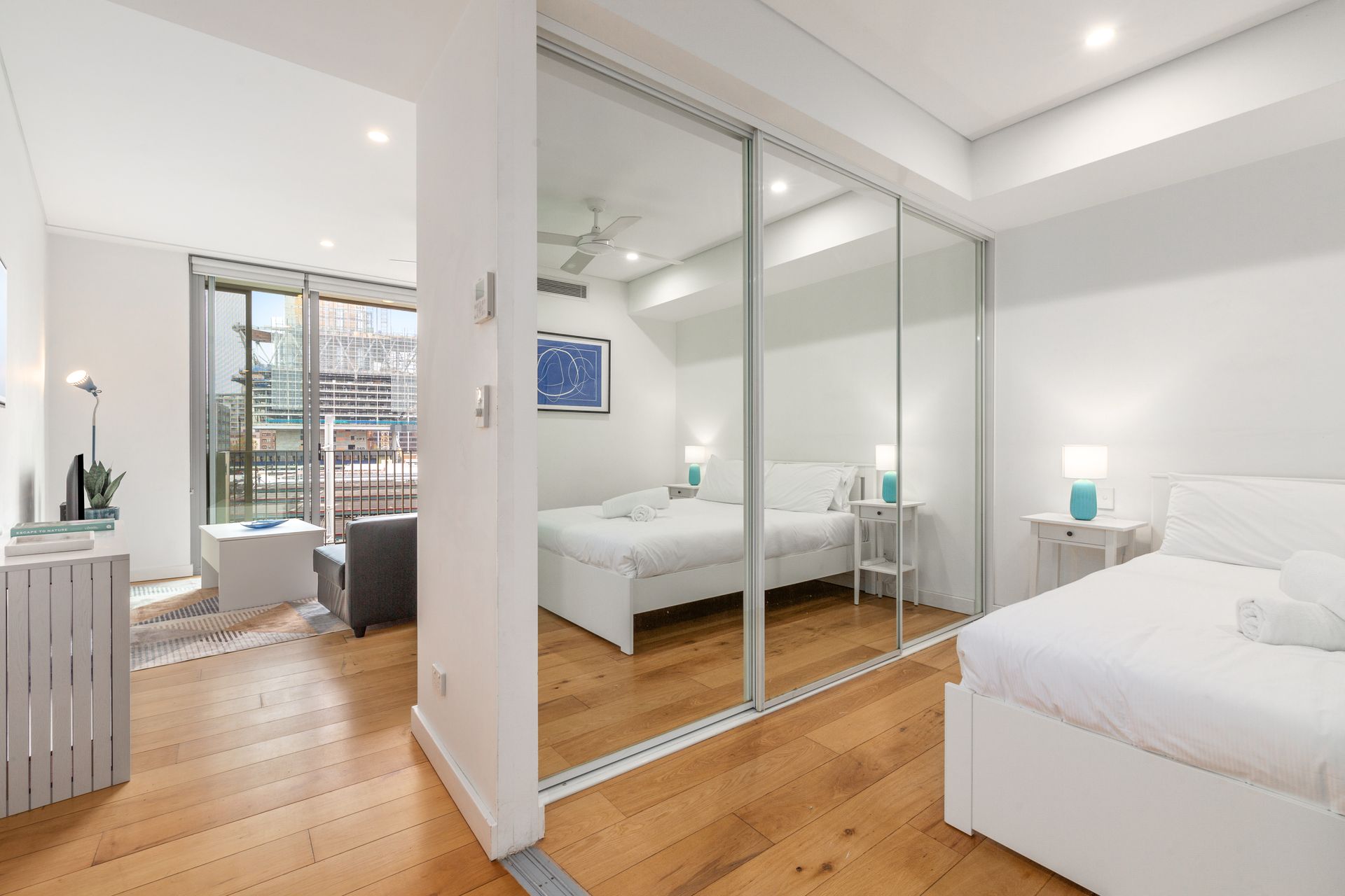 Bright modern bedroom with mirrored closet doors, white bedding, and wood floors