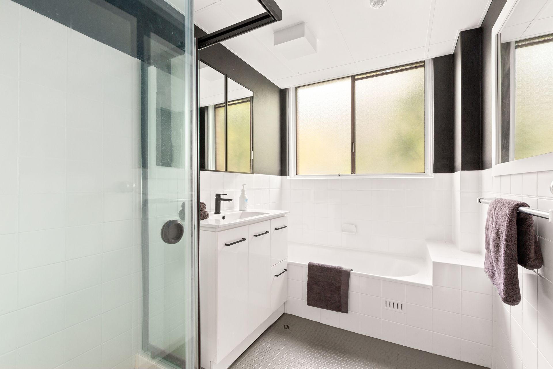 Bright modern bathroom with glass shower, white vanity, and windowed tub alcove