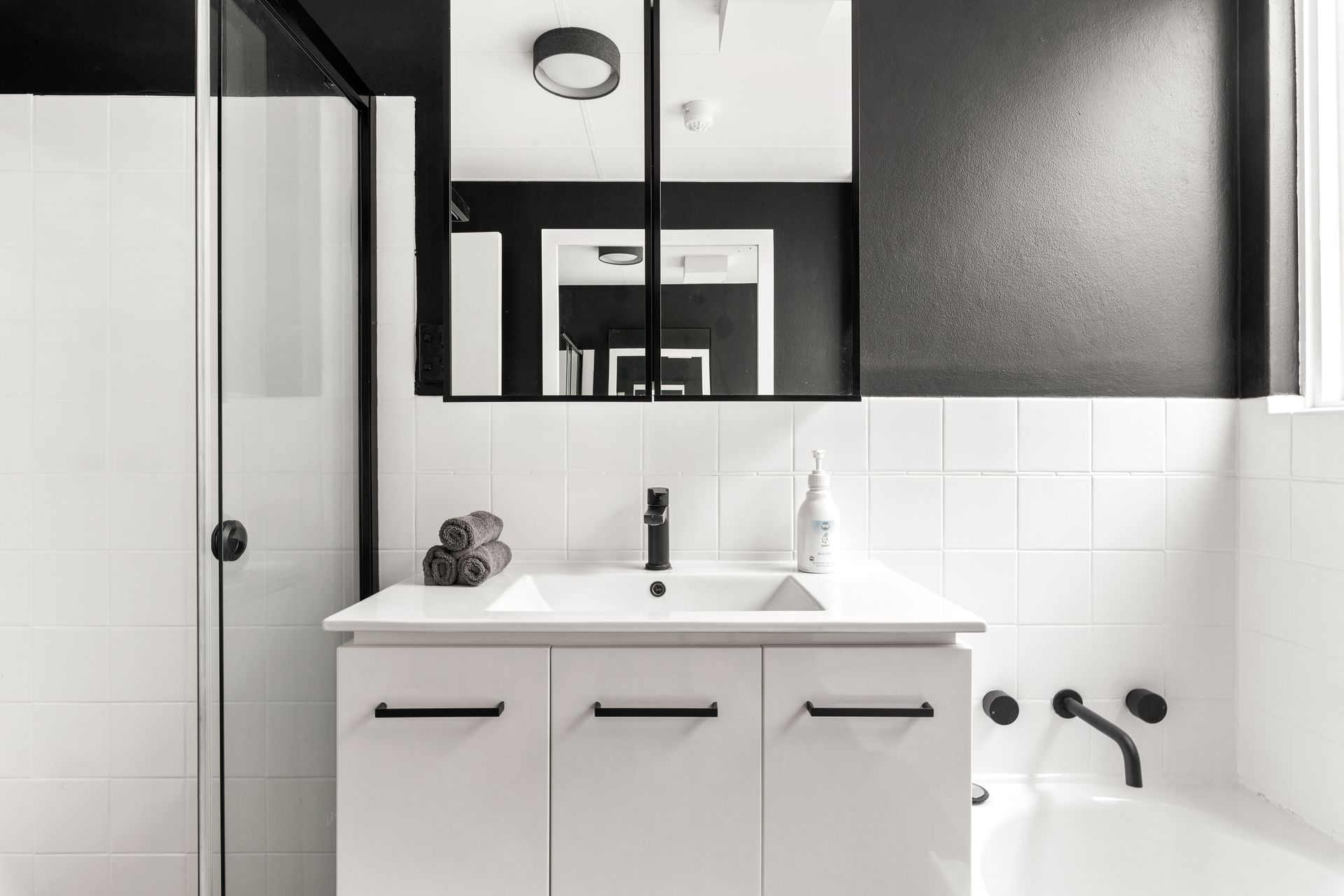 Modern black-and-white bathroom with vanity, mirror cabinet, shower, and bathtub