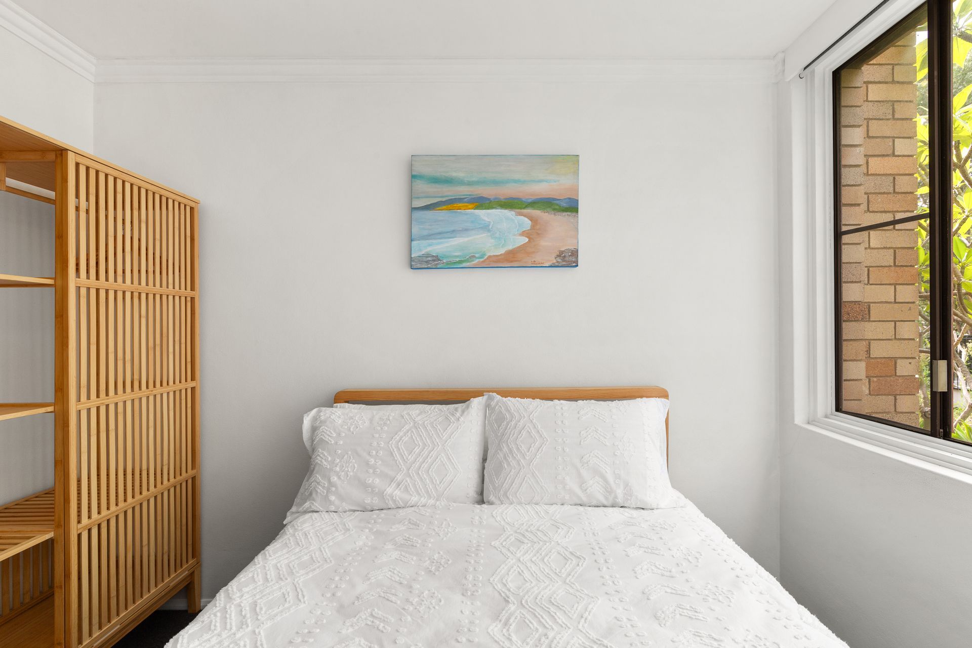 Bright bedroom with a white bed, wooden room divider, wall art, and a window letting in daylight