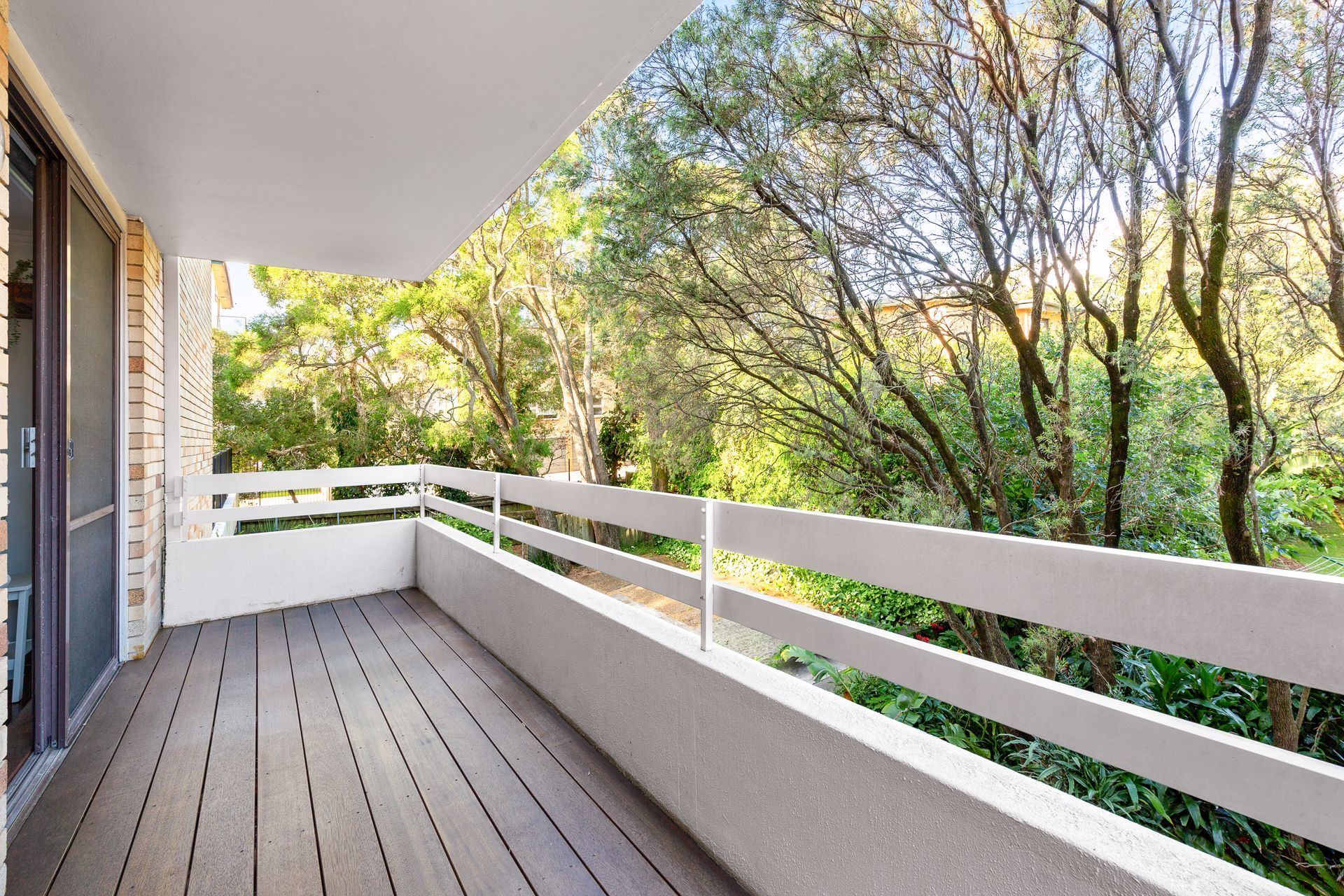 Covered balcony with gray deck, white railing, and trees beyond.