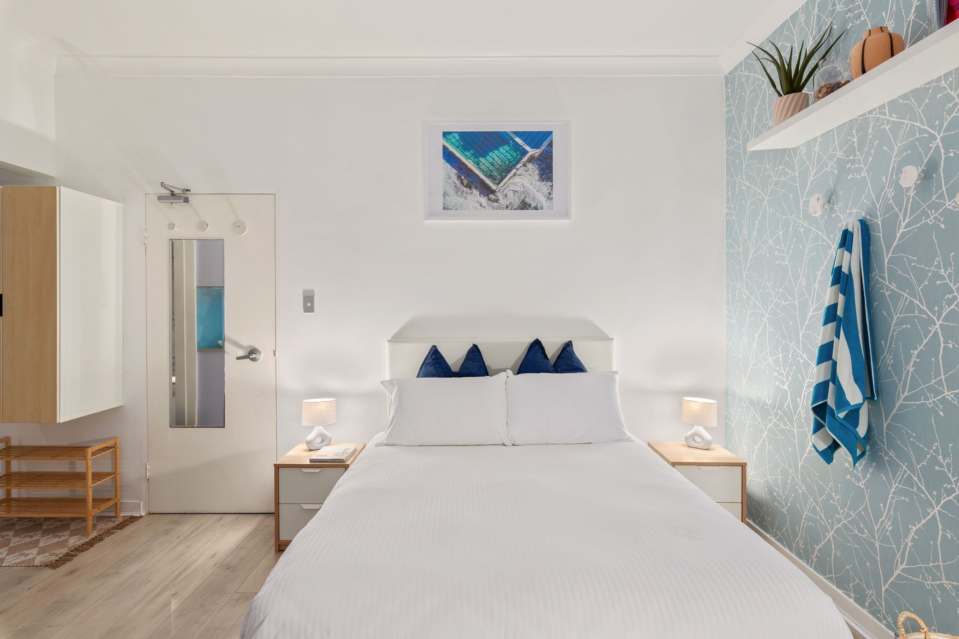Bright white bedroom with blue accents, twin beds, and a tropical mural on the right wall.