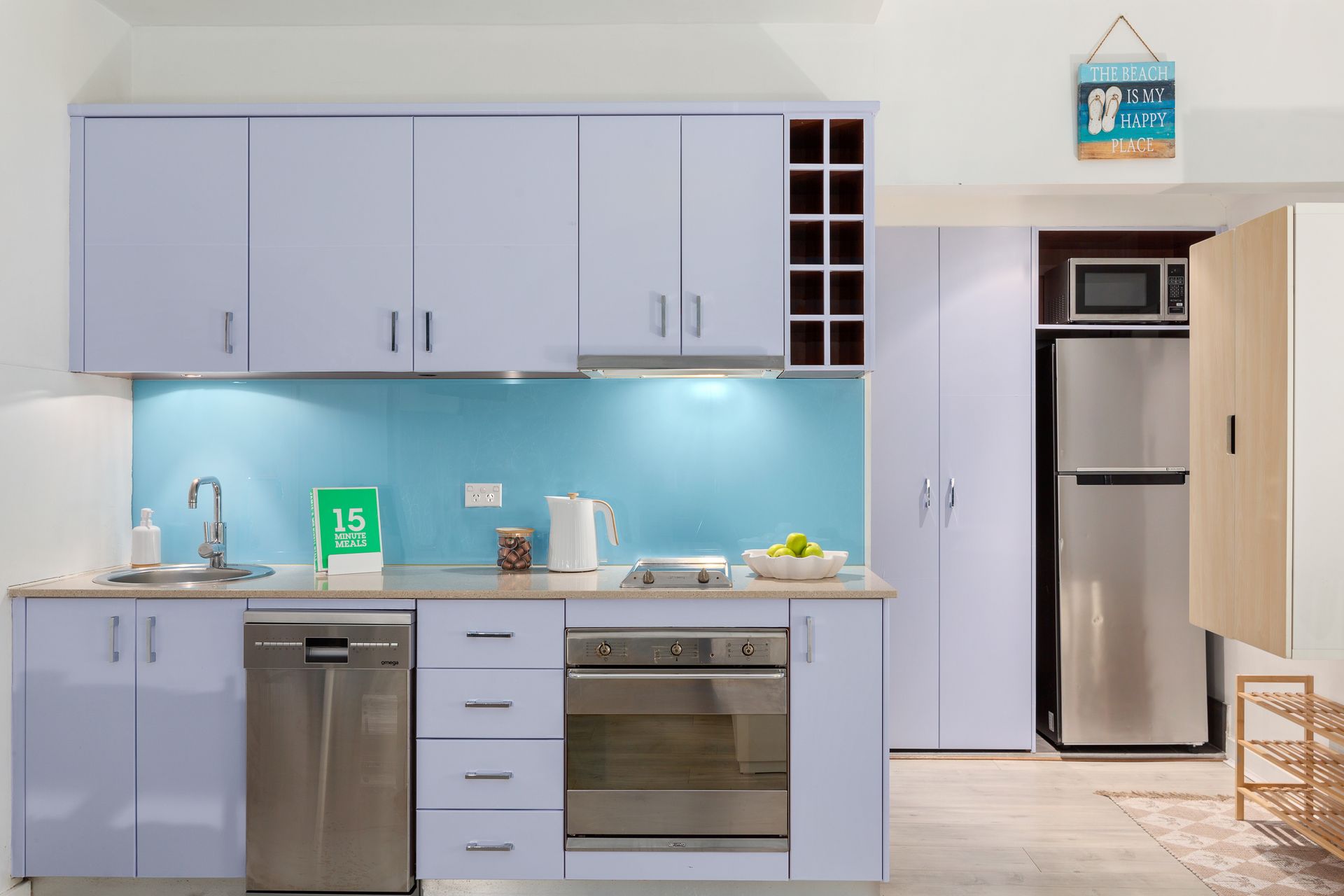 Modern kitchen with pale blue cabinets, stainless appliances, and a light wood pantry door