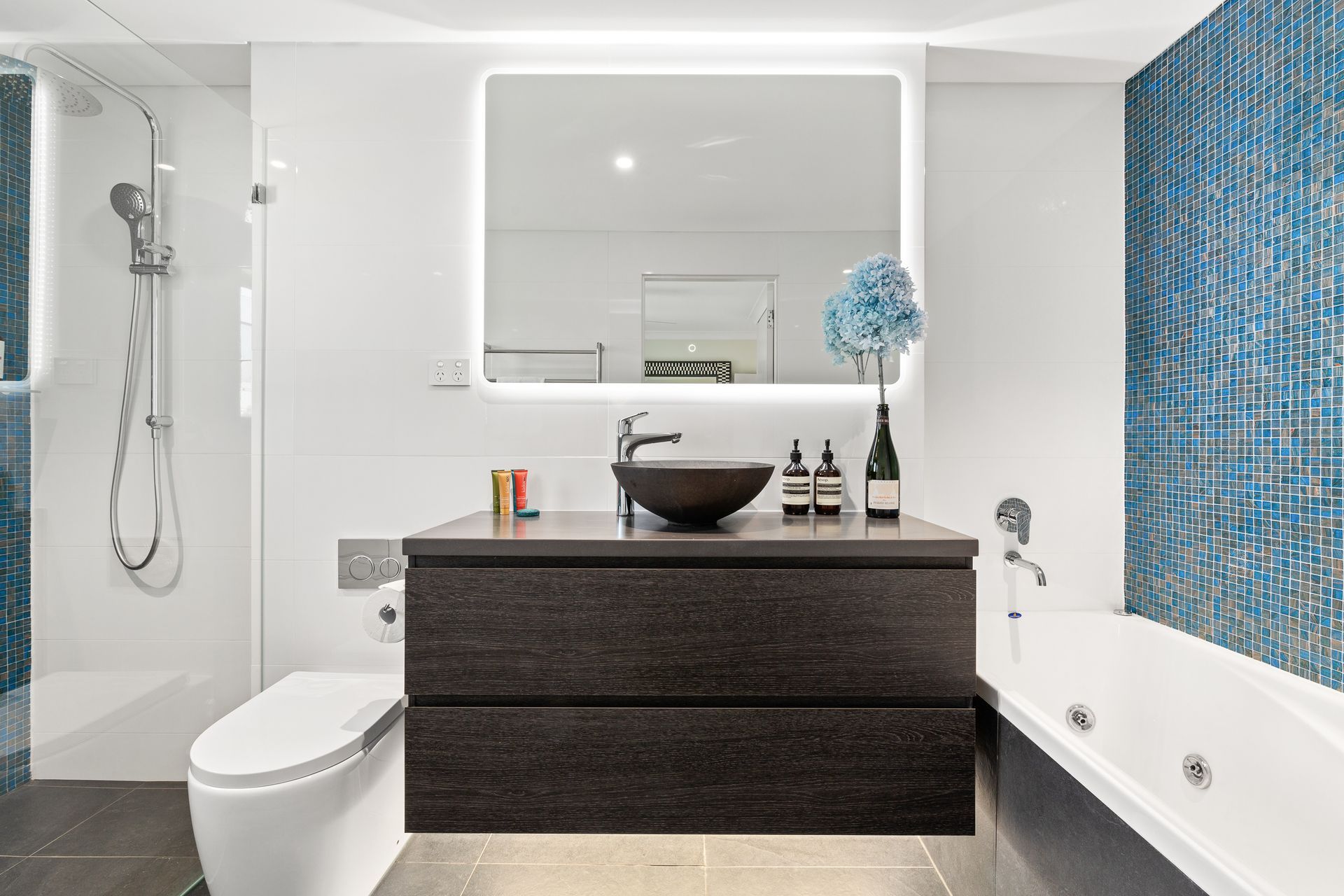 Modern bathroom with dark vanity, wall mirror, shower, and blue mosaic accent tiles