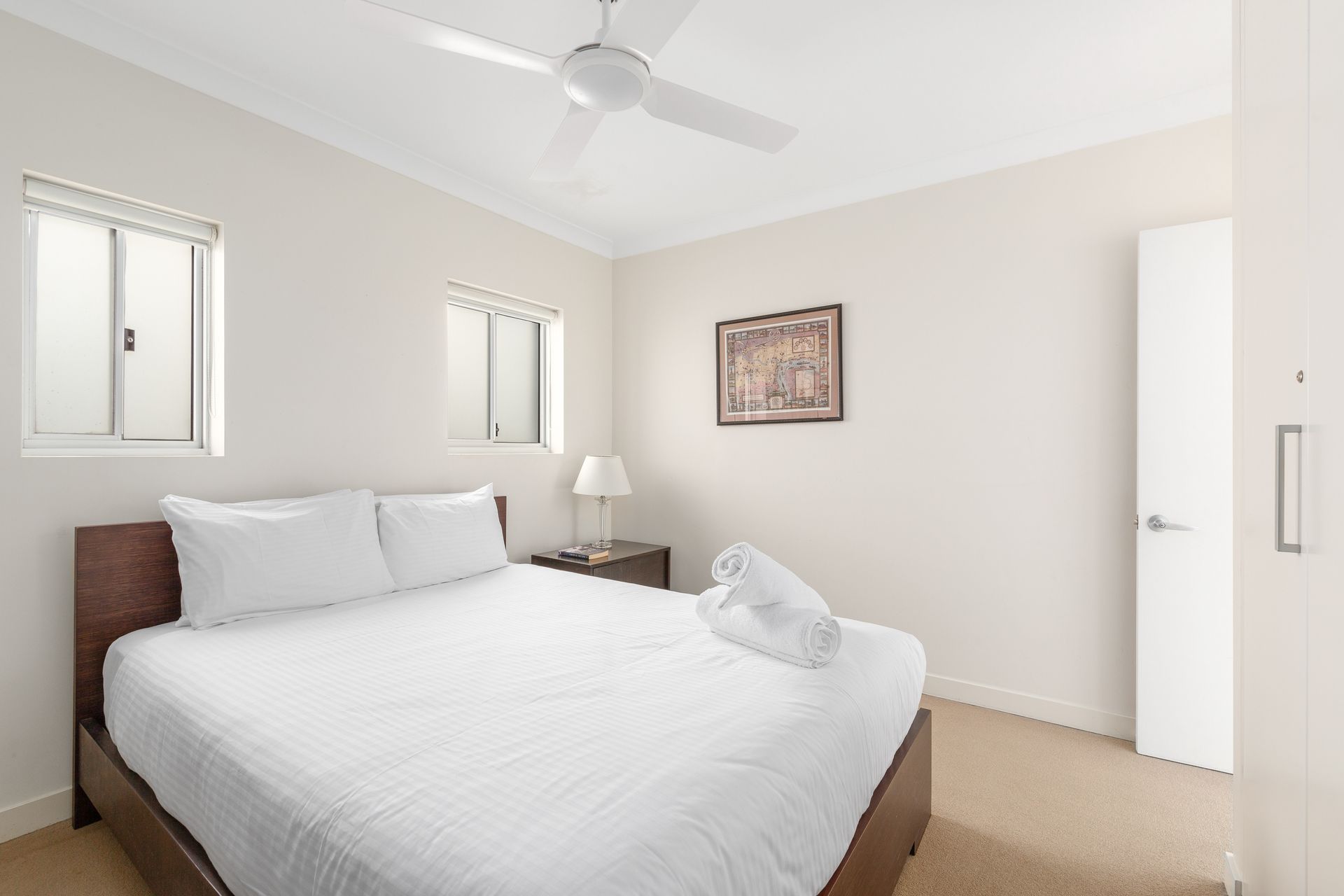 Bright bedroom with a white bed, ceiling fan, bedside lamp, and beige walls