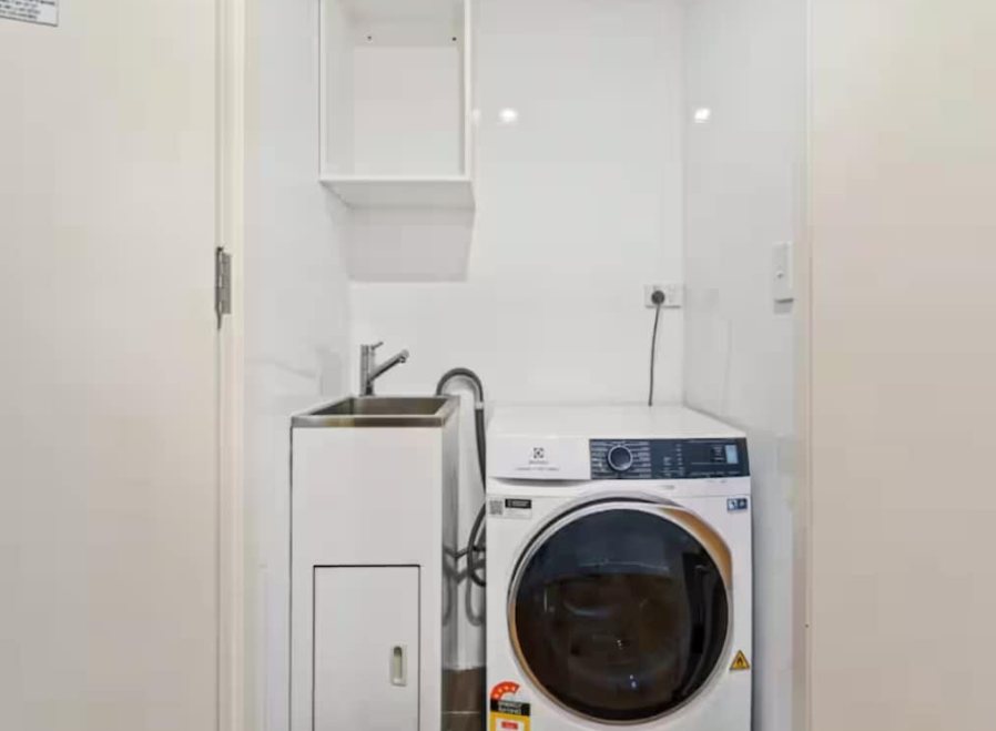 Compact laundry room with a sink cabinet, wall shelves, and a front-loading washing machine