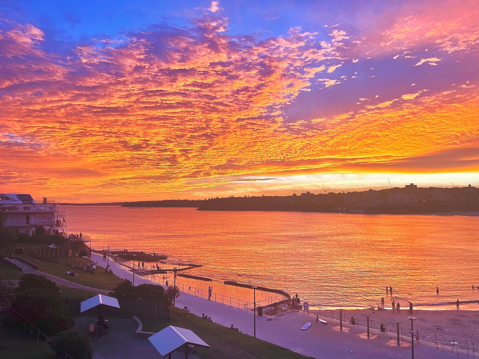 Sunset over a riverside beach with orange clouds and people along the shore