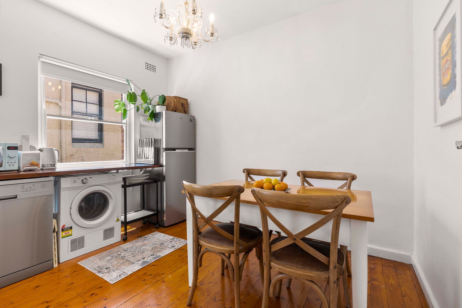 Bright dining nook with wooden table, chairs, and a small kitchen with washer and gray cabinets.