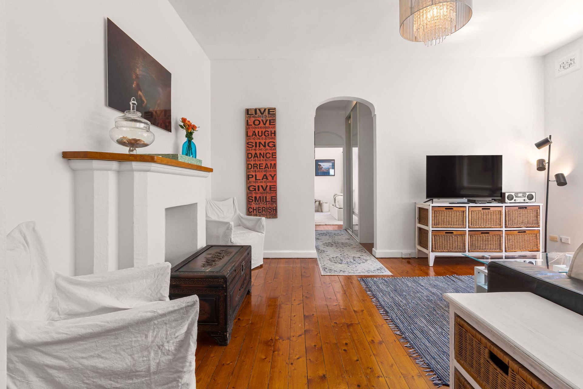 Bright living room with wood floors, white walls, fireplace, TV, and blue rug