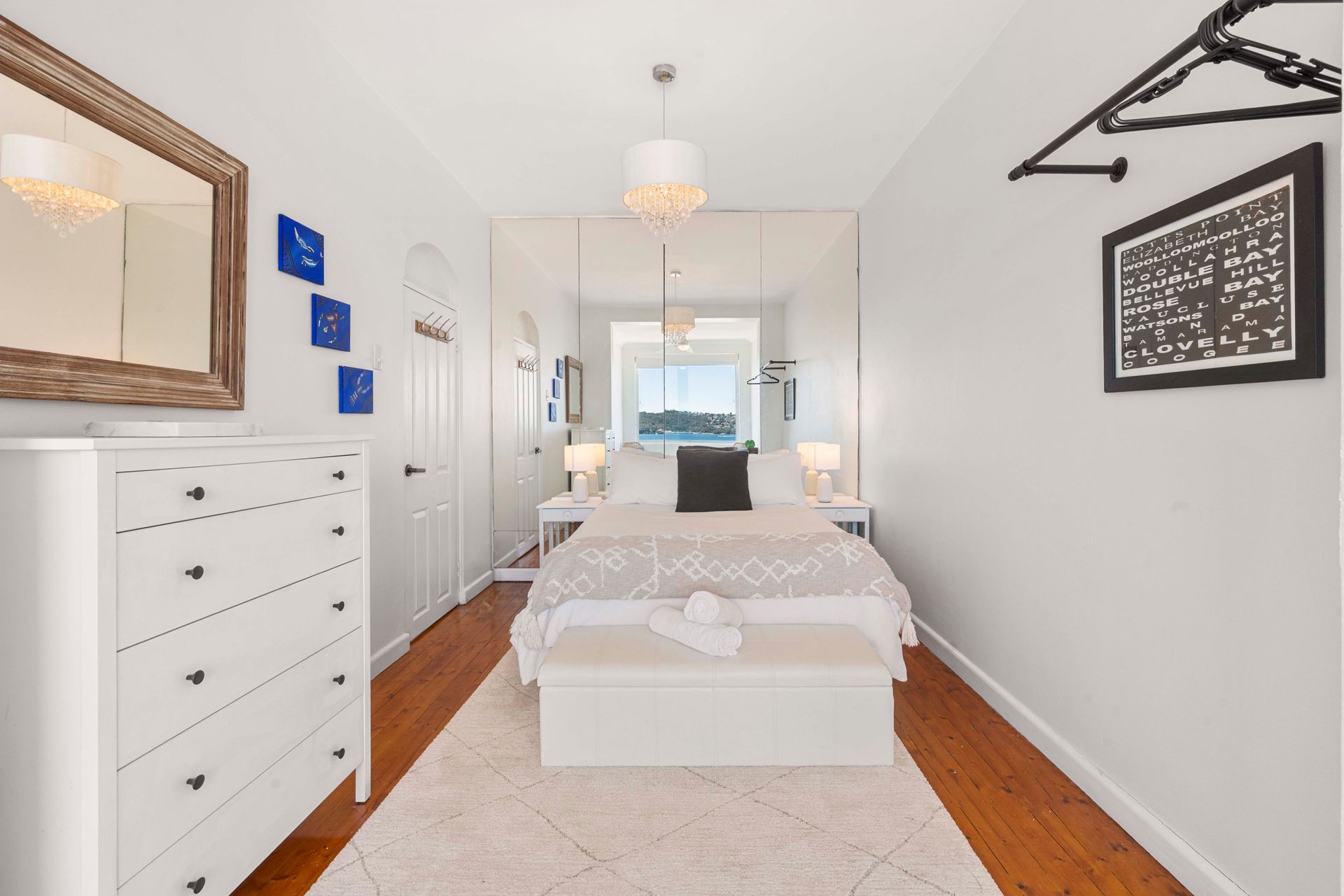 Bright white bedroom with a bed, dresser, mirror, and framed wall art, viewed from the doorway