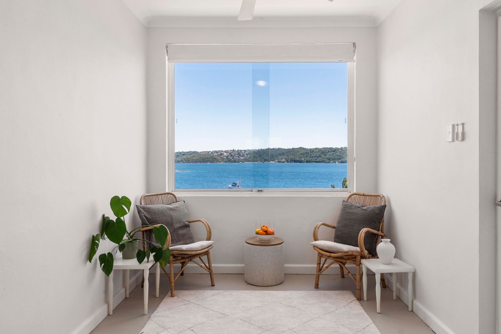 Bright seaside sitting area with two wicker chairs, small table, and ocean view through a large window