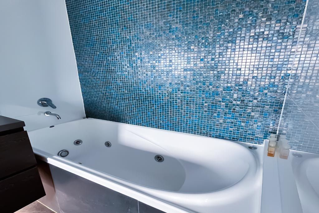 Modern bathroom with a white bathtub, dark vanity, and blue mosaic tile wall