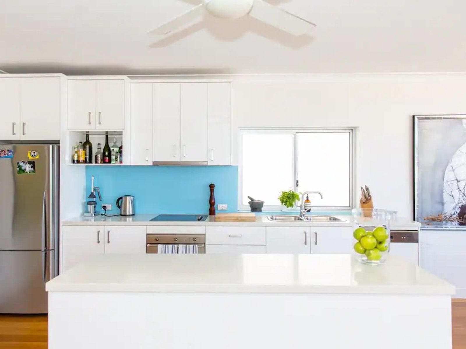 Bright modern kitchen with white cabinets, blue backsplash, stainless fridge, and an island with fruit bowl