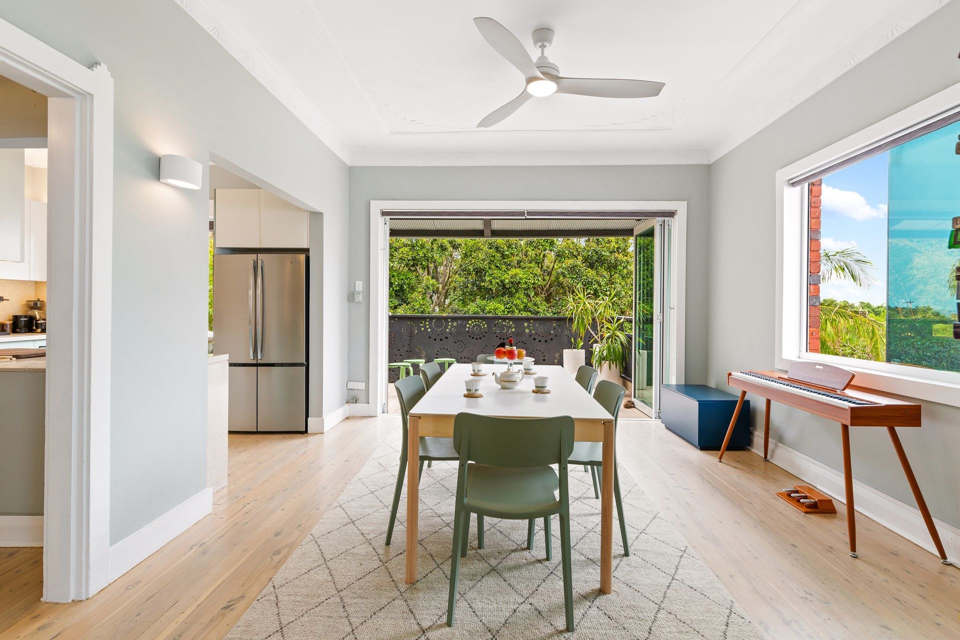 Bright dining room with table, chairs, rug, ceiling fan, and open doors to a green patio.