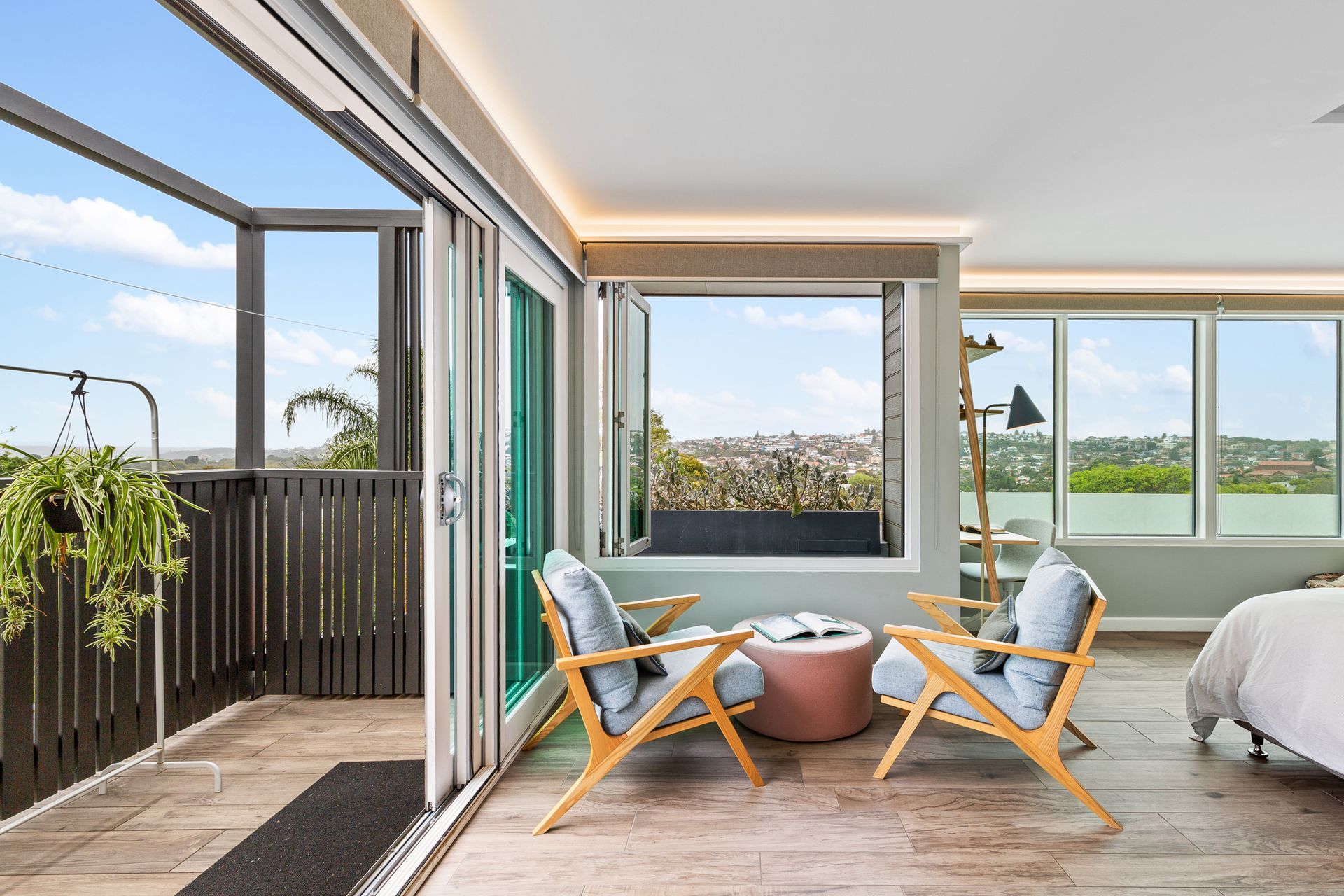 Bright balcony with two lounge chairs, round table, open doors, and a view of greenery and water