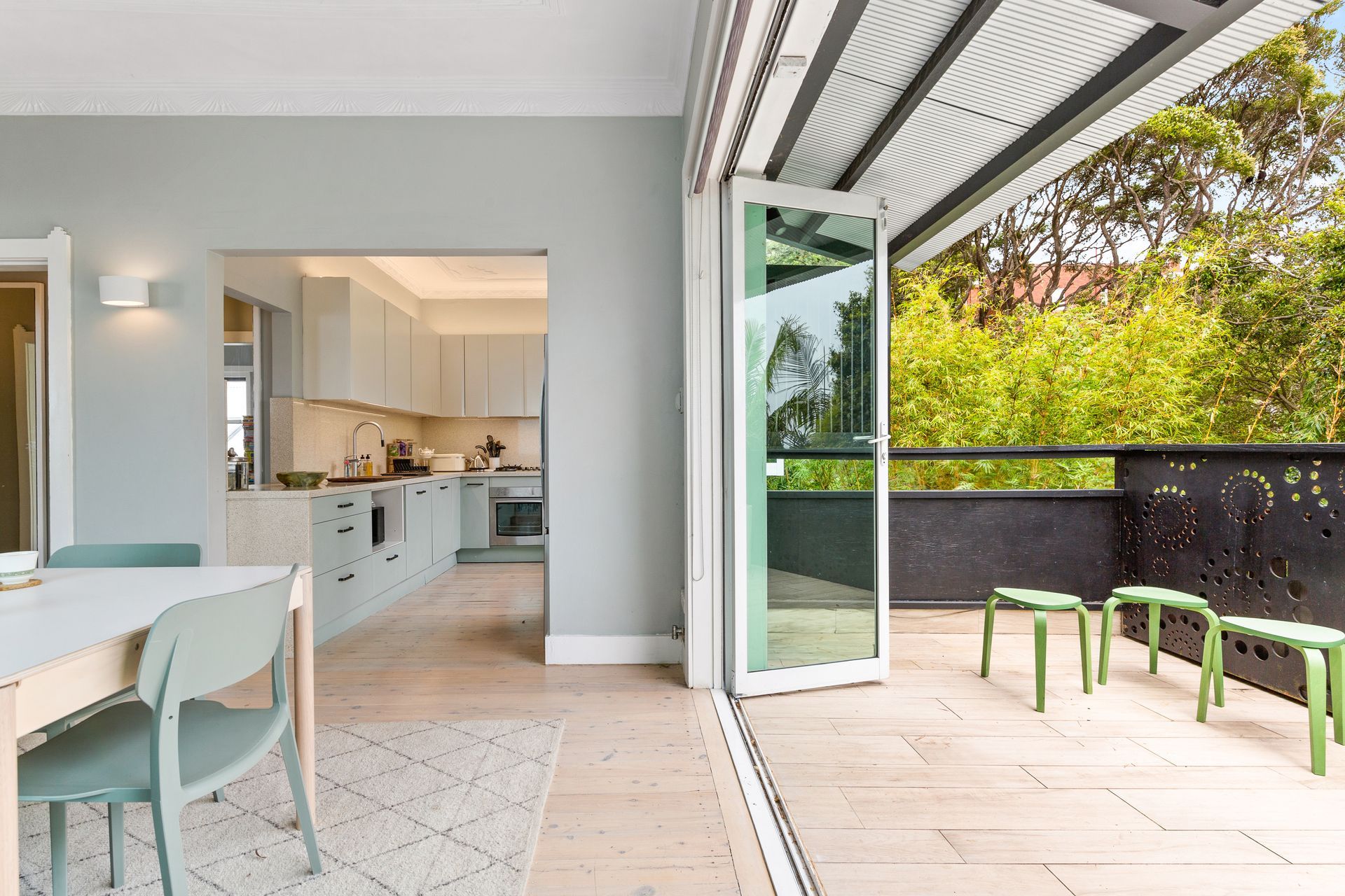 Bright modern dining area opening to a tiled patio with open glass doors and green chairs.