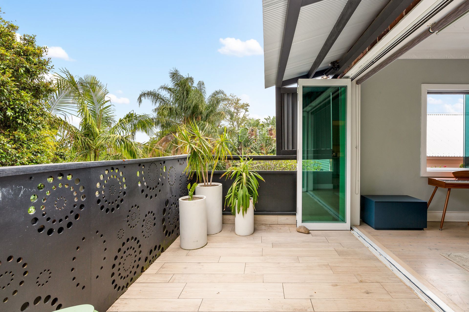 Modern balcony with patterned railing, potted plants, green glass door, and outdoor seating area