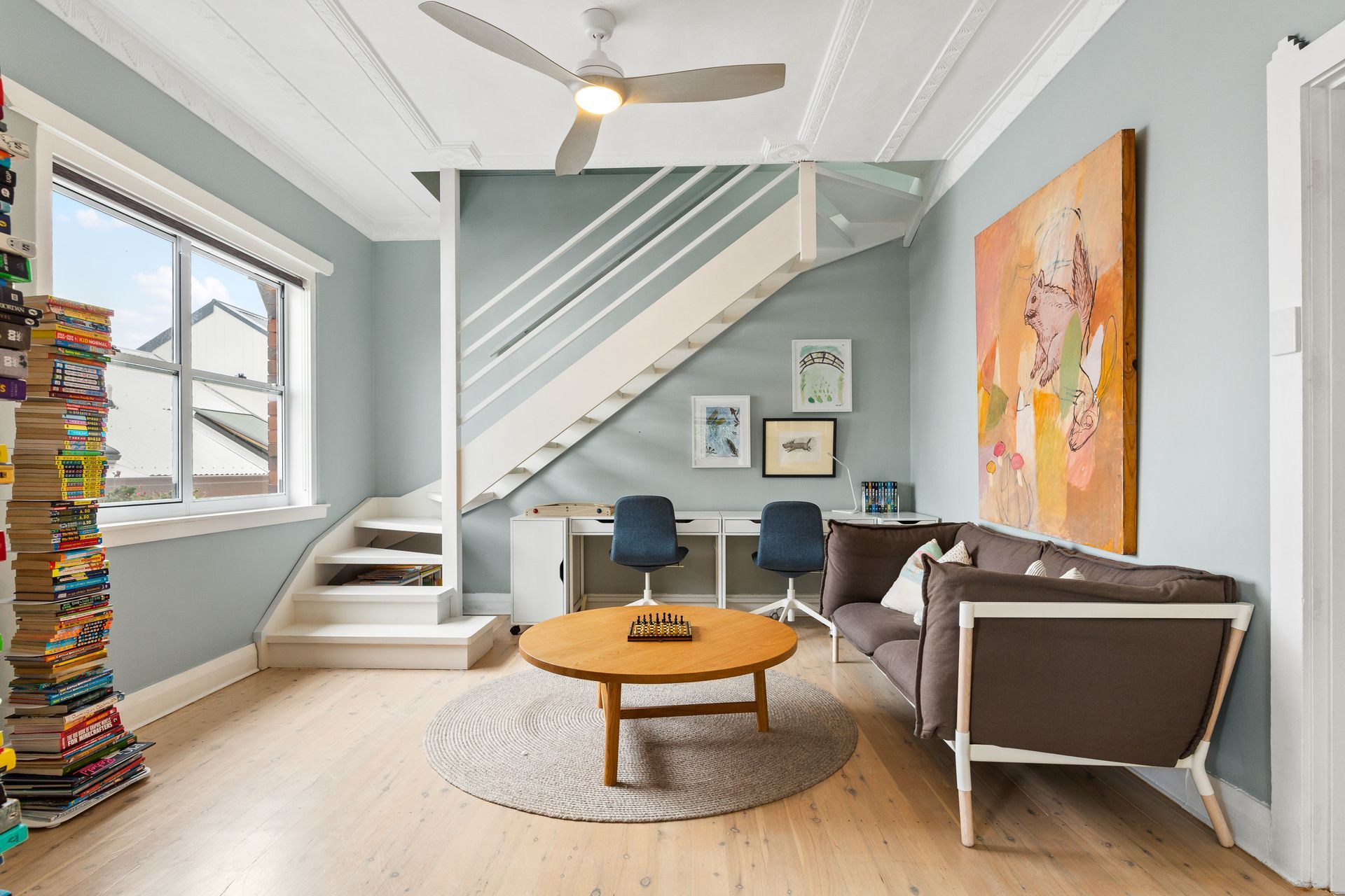 Bright living room with stairs, teal accent wall, brown sofa, round coffee table, and abstract art