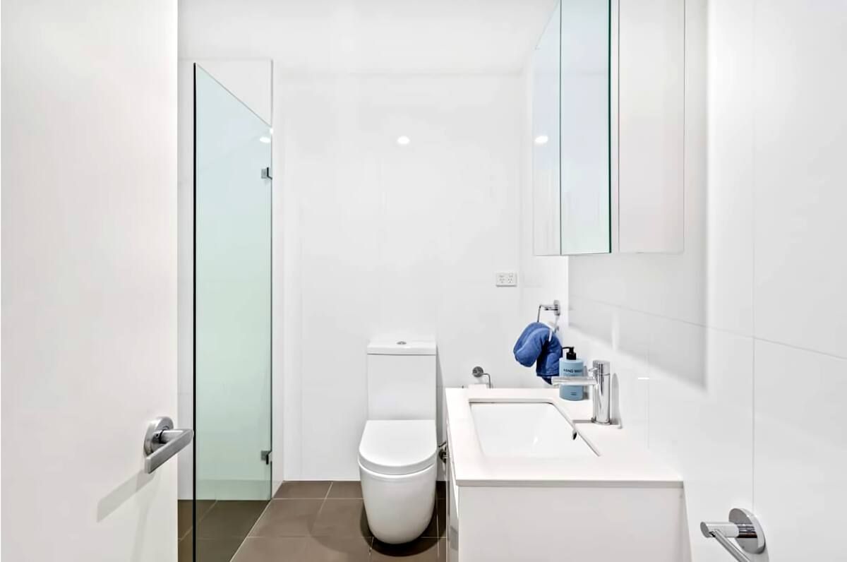 Bright white modern bathroom with toilet, sink vanity, and glass shower door