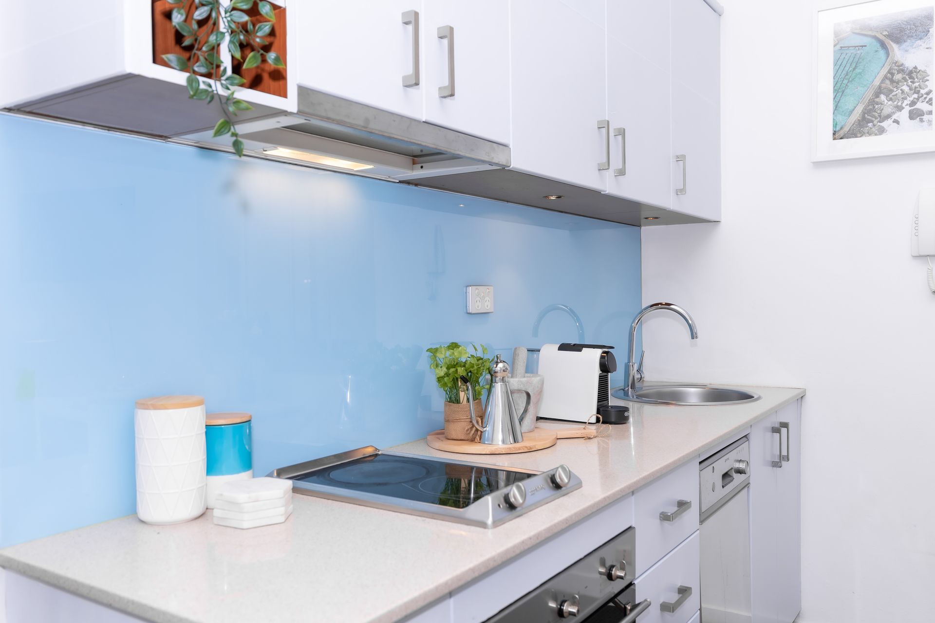 Modern white kitchen with blue backsplash, stove, sink, cabinets, and countertop items