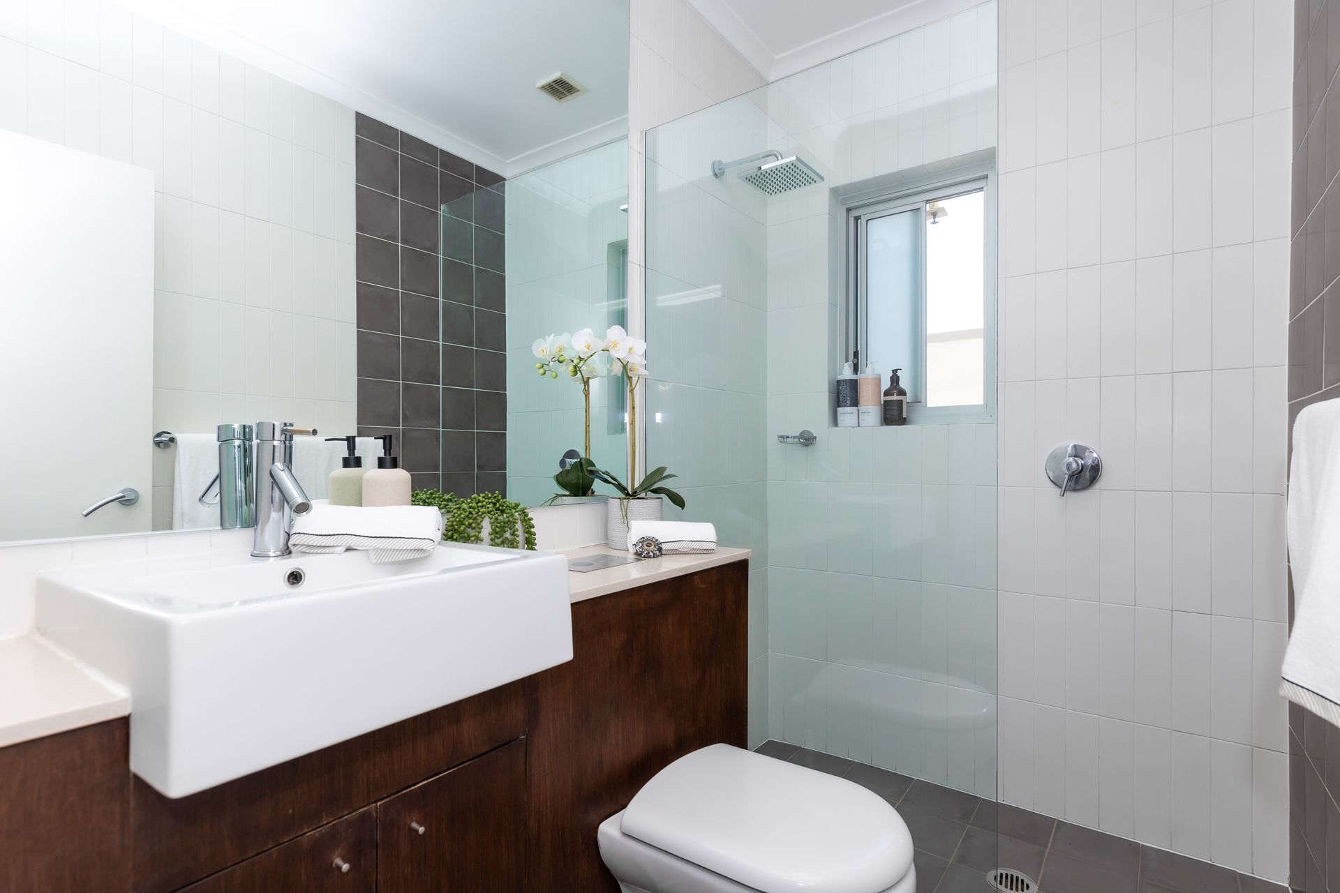 Modern white bathroom with wall-mounted sink, toilet, wooden vanity, and glass shower enclosure