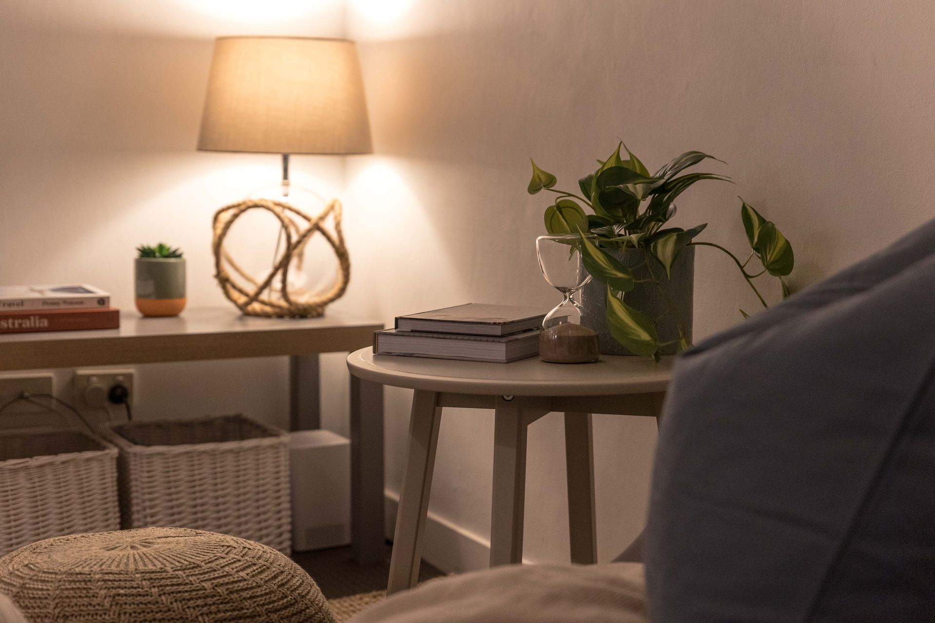 Cozy living room corner with a lit table lamp, side table, potted plant, and sofa in warm light